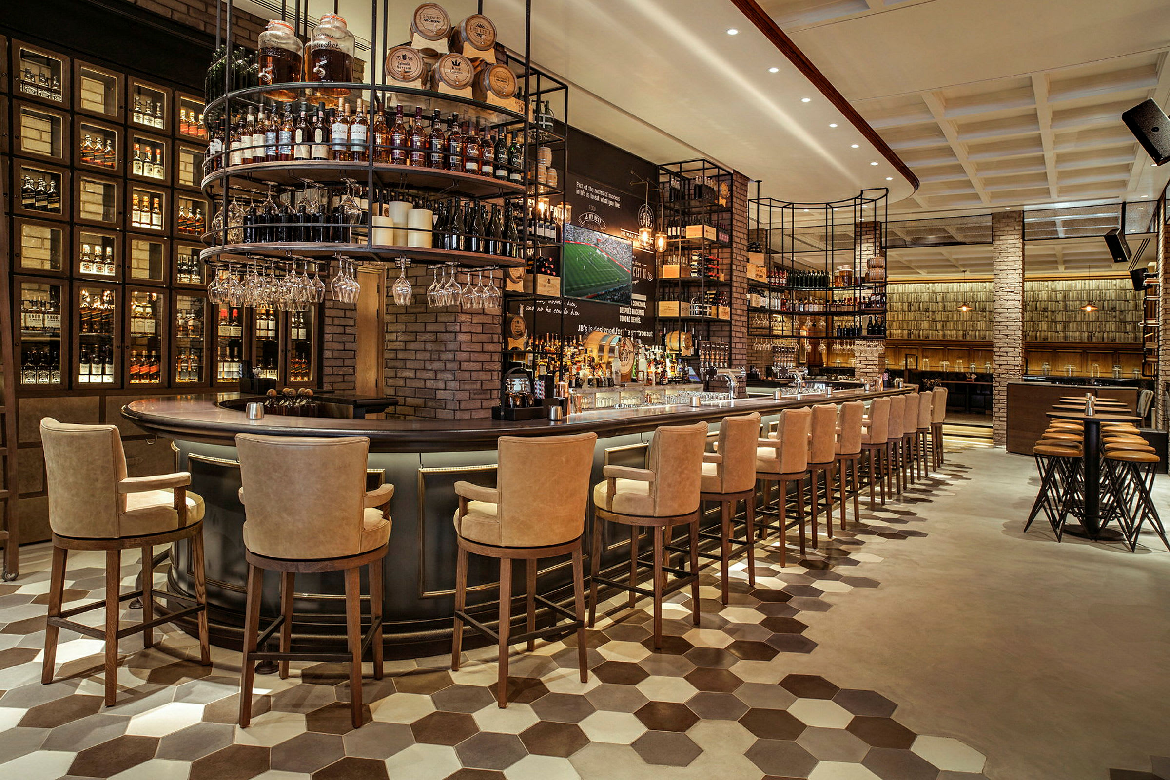 Billede af interiøret i en moderne bar med højryggede stole ved en stor bardisk omgivet af hylder fyldt med flasker og tønder. (AI-genereret tekst)