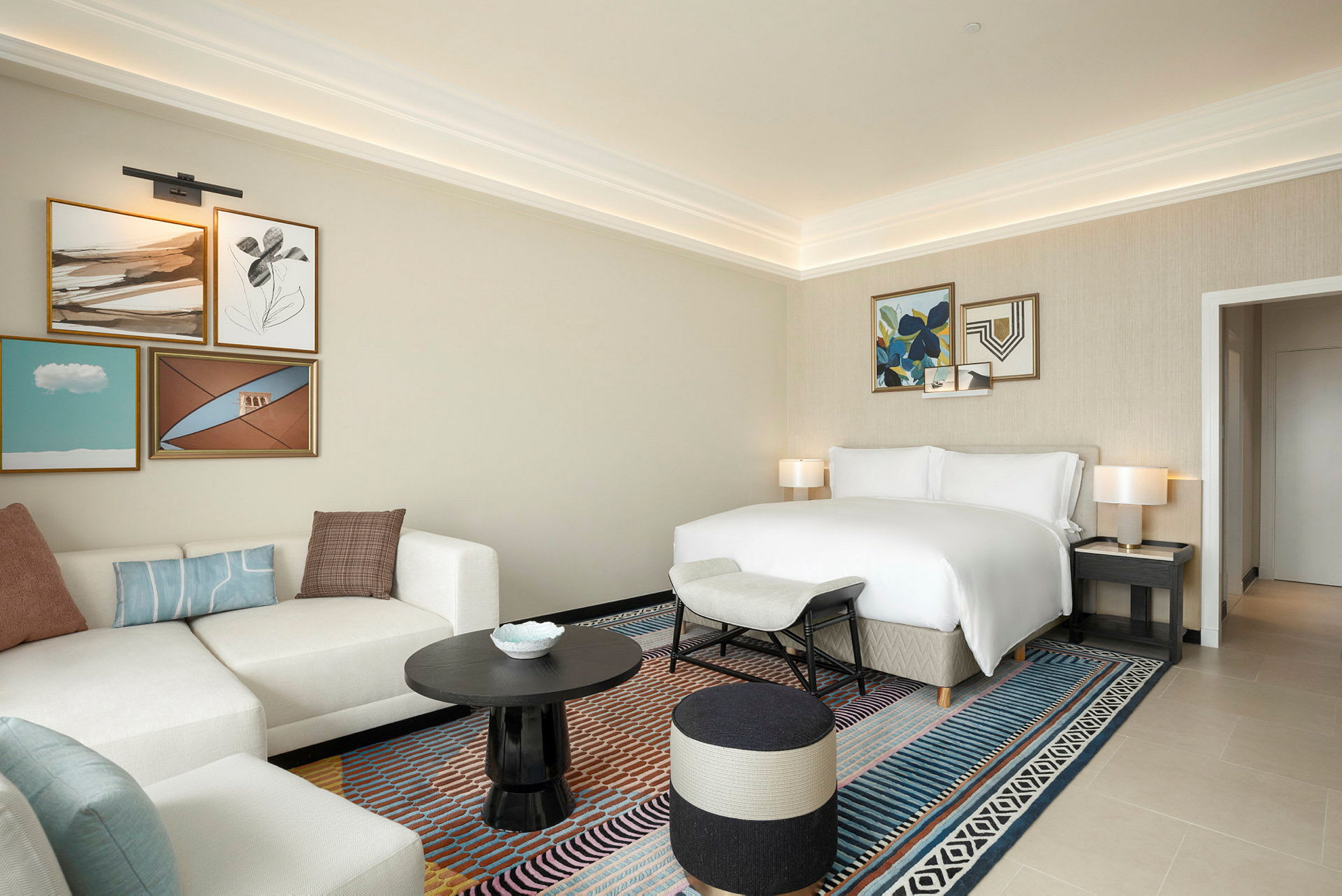 Hotelværelse med lys indretning, sofa, seng og kunst på væggene. (AI-genereret tekst)