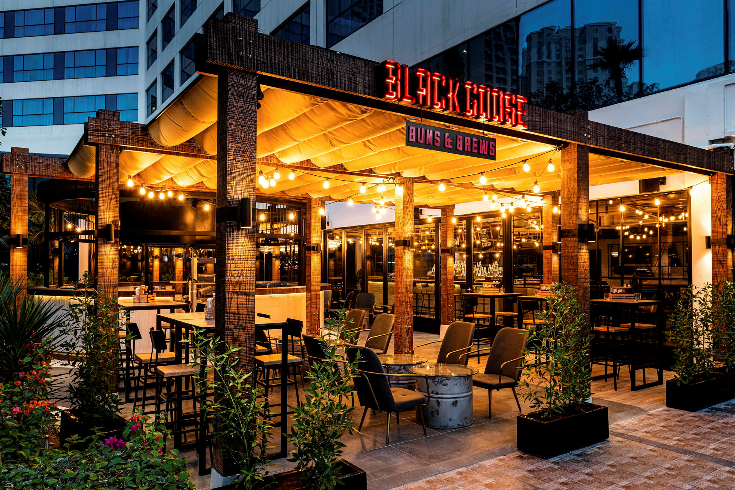 Billede af en udendørsrestaurant med navnet 'Black Goose', oplyst og dekorativt med møbler og planter. (AI-genereret tekst)