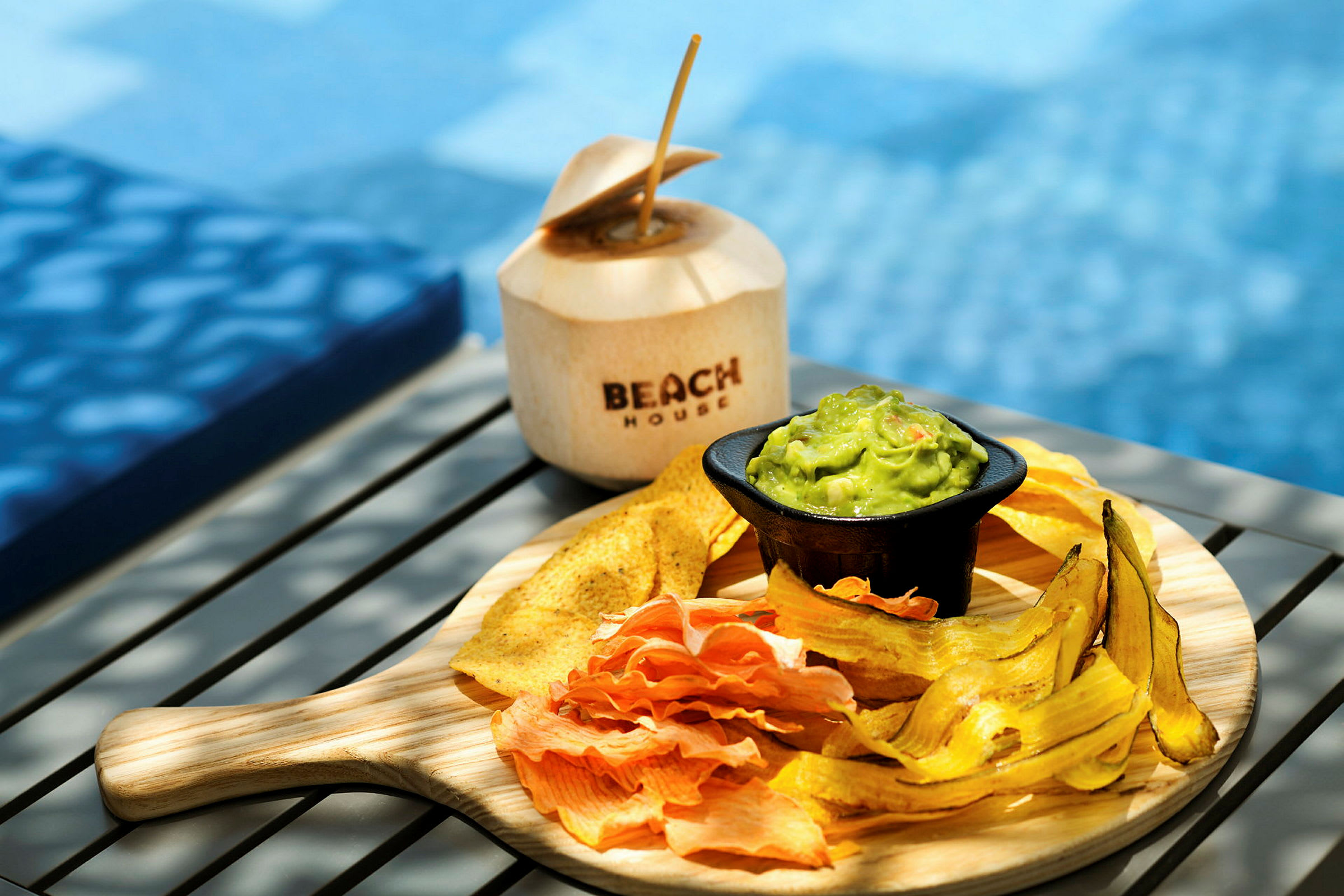 En tallerken med forskellige chips og guacamole samt en kokosnød med teksten 'Beach House'. (AI-genereret tekst)