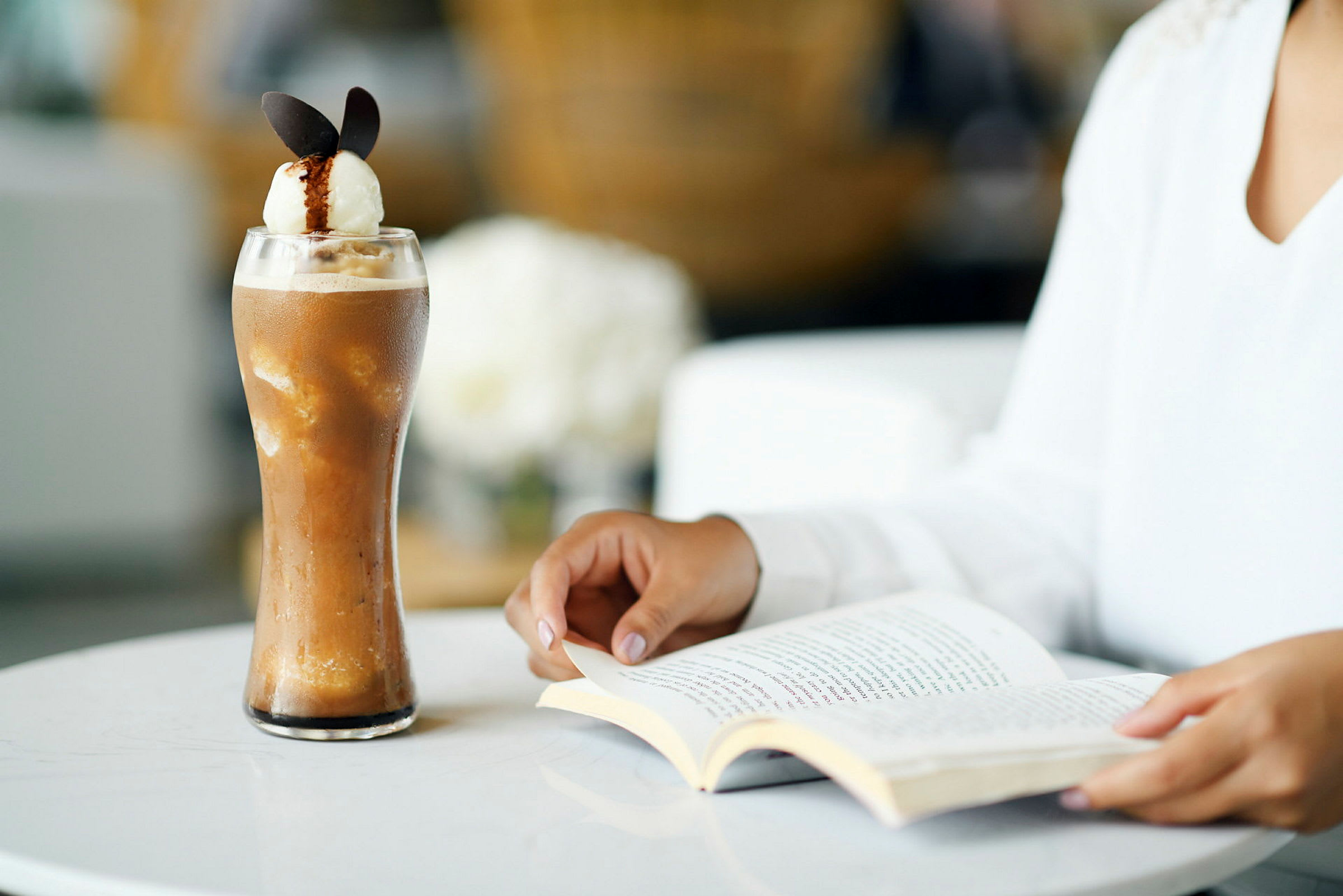 Et glas med kold kaffedrik og en person, der læser en bog ved en bord. (AI-genereret tekst)