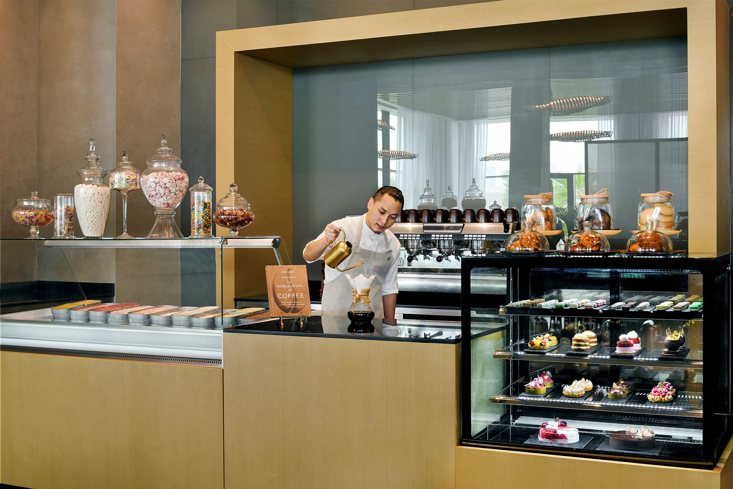 En kaffestation med glasdisplayskab fyldt med kager og ingredienser. (AI-genereret tekst)