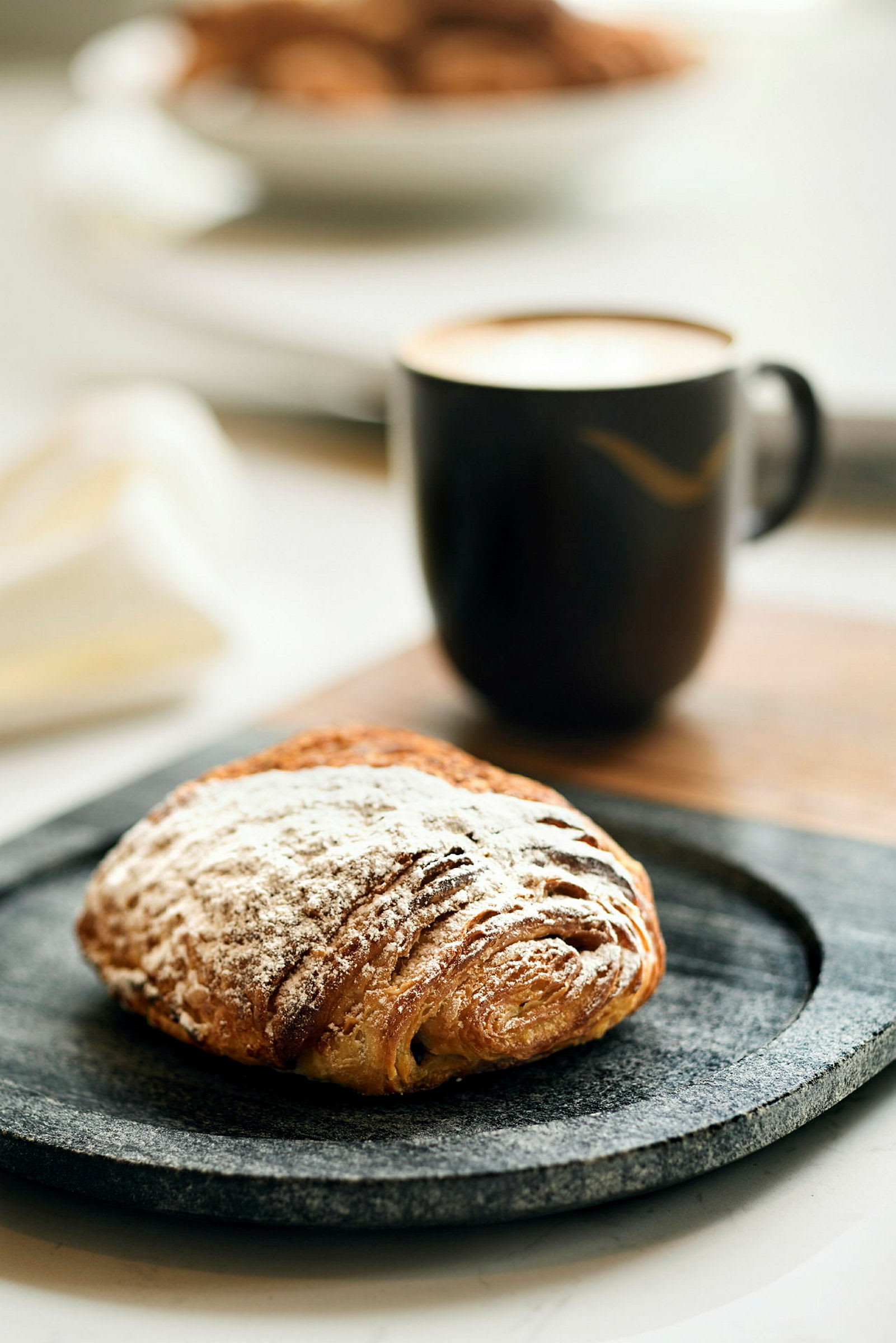 En kop kaffe og en bolle med flormelis på en tallerken. (AI-genereret tekst)