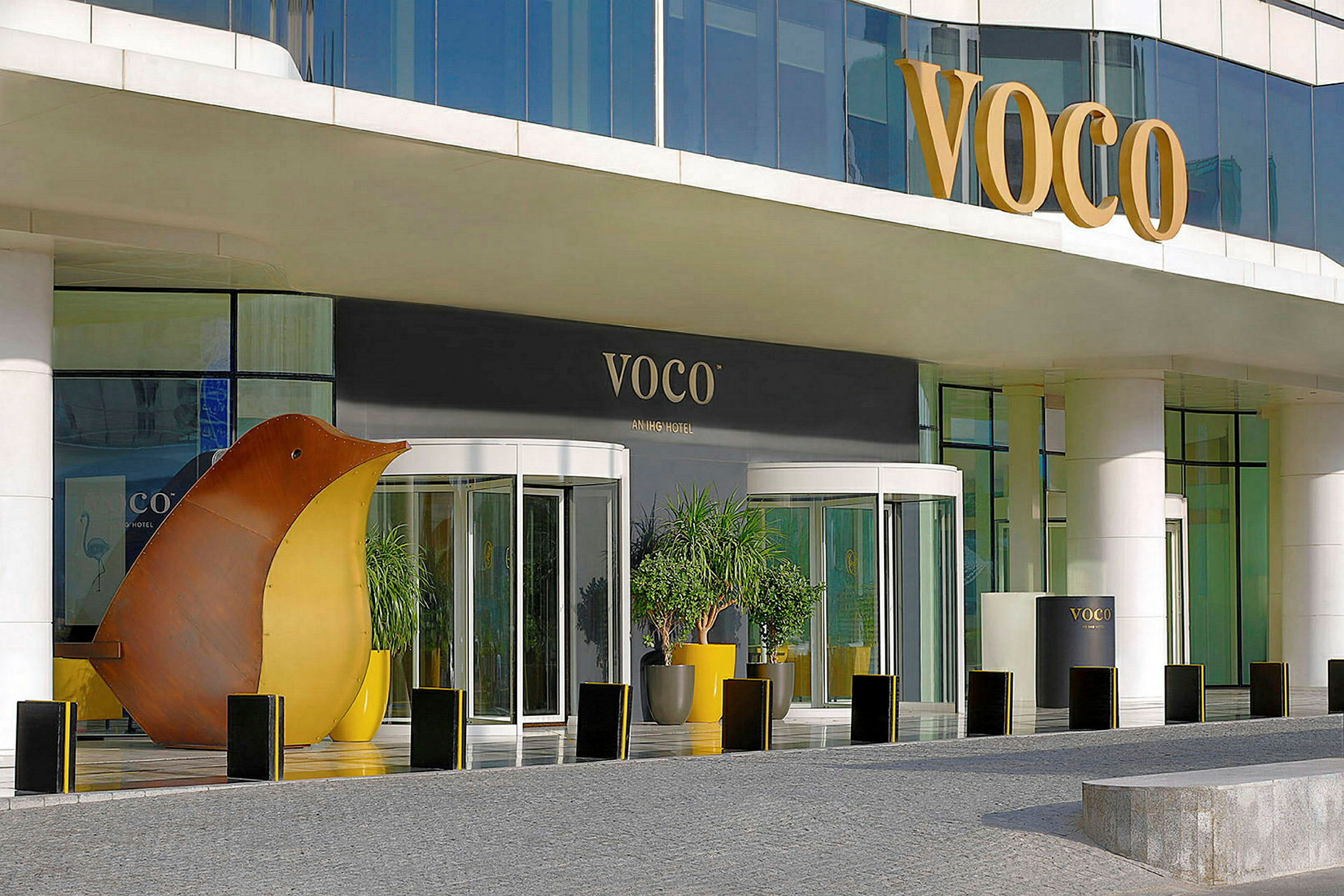 Indgang til et hotel med glasdøre og skiltet 'VOCO' samt dekorationer og planter. (AI-genereret tekst)