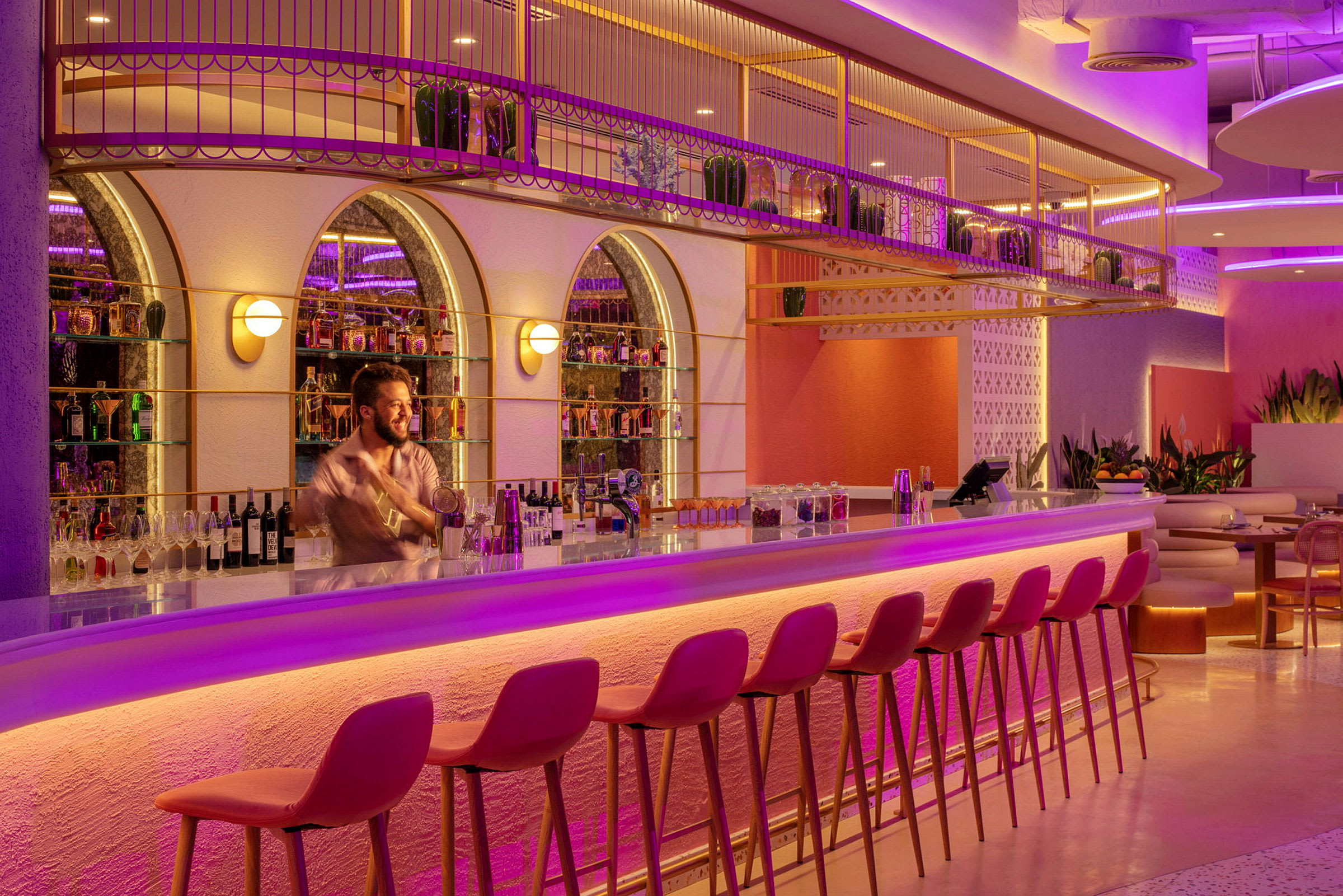 En elegant bar med lyserød og lilla belysning, høje stole og flasker på hylder. (AI-genereret tekst)