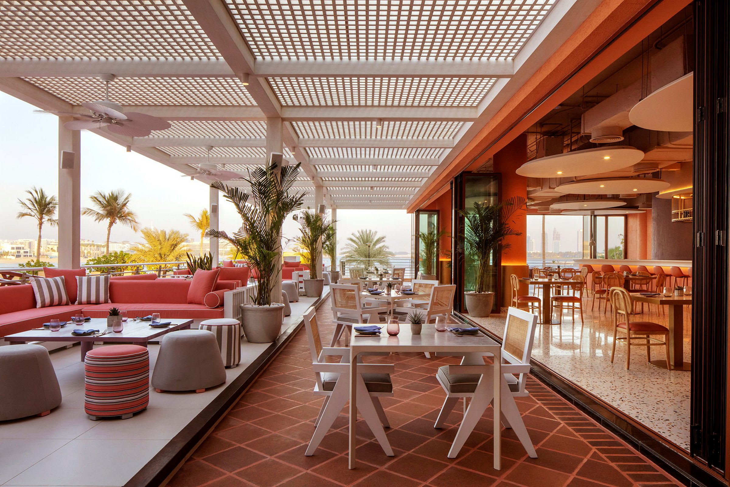 En åben terrasse på en restaurant med siddegrupper og borde, omgivet af palmer og en luftig atmosfære. (AI-genereret tekst)