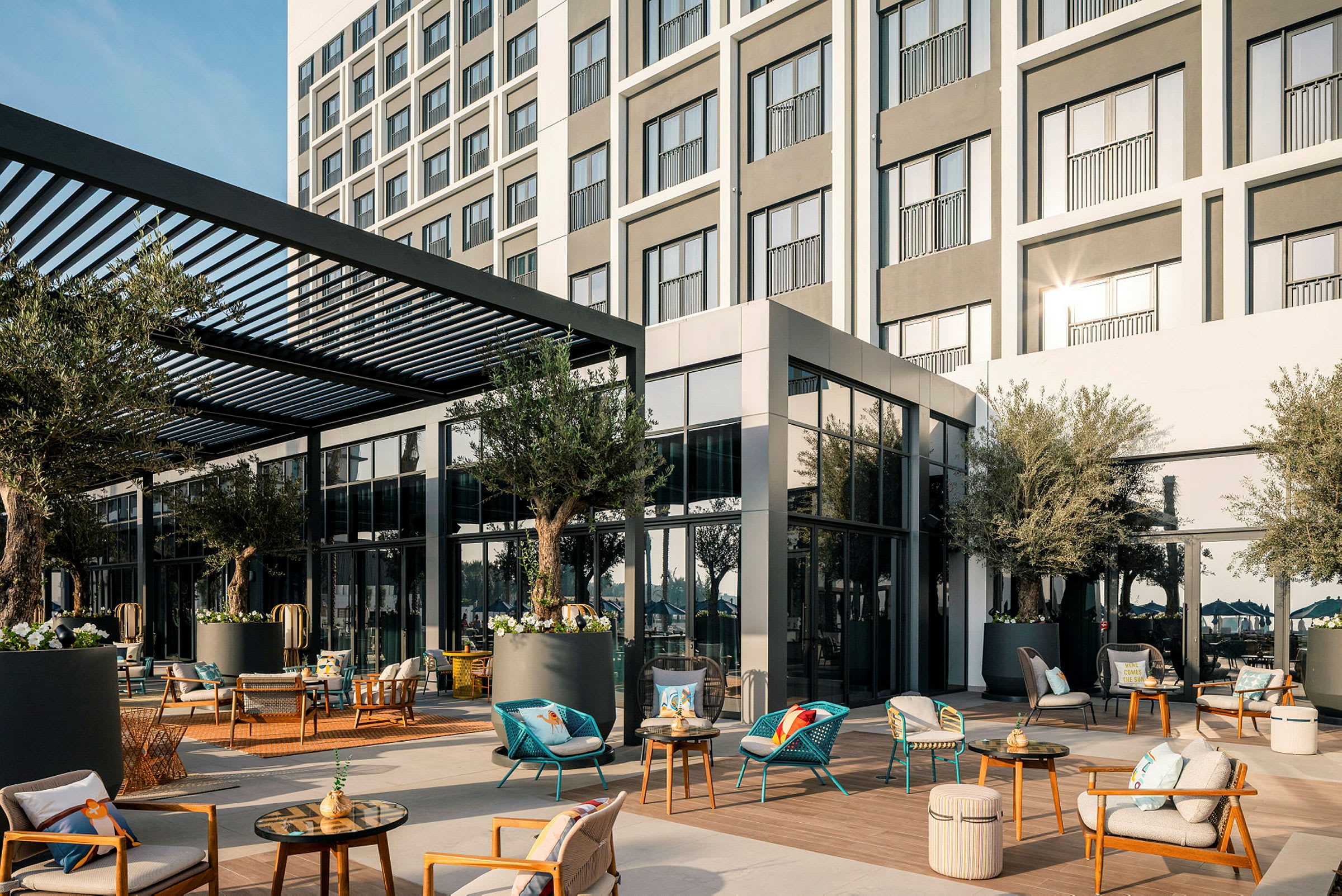 Hotelfacade med møbleret terrasse, skygget af en pergola, omgivet af planter. (AI-genereret tekst)
