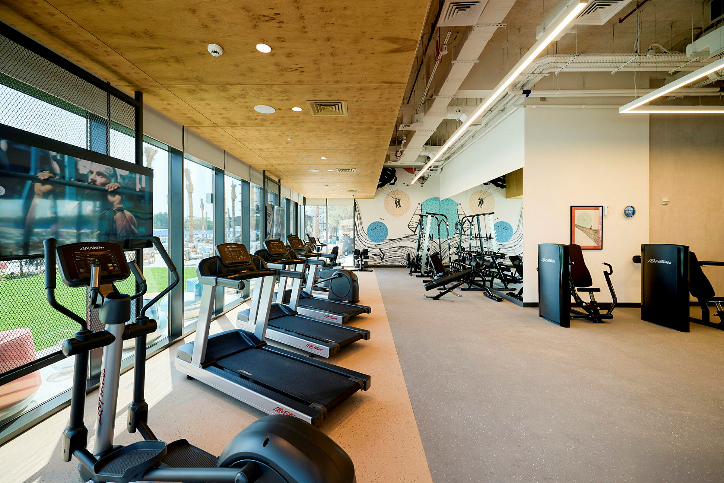 Billede af et fitnesscenter med løbebånd, træningsmaskiner og store vinduer. (AI-genereret tekst)