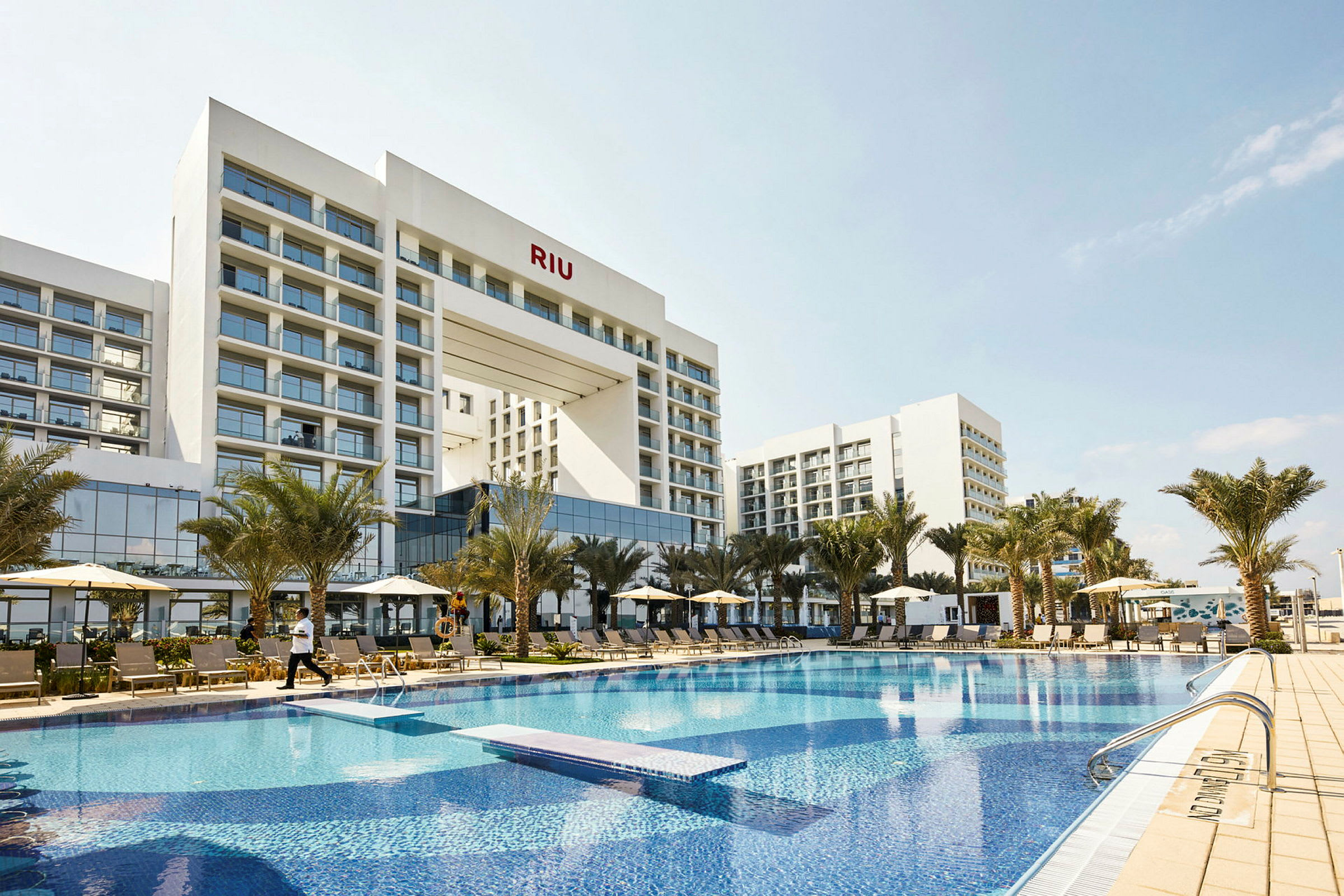 Hotelbygning med swimmingpool og liggestole foran. (AI-genereret tekst)