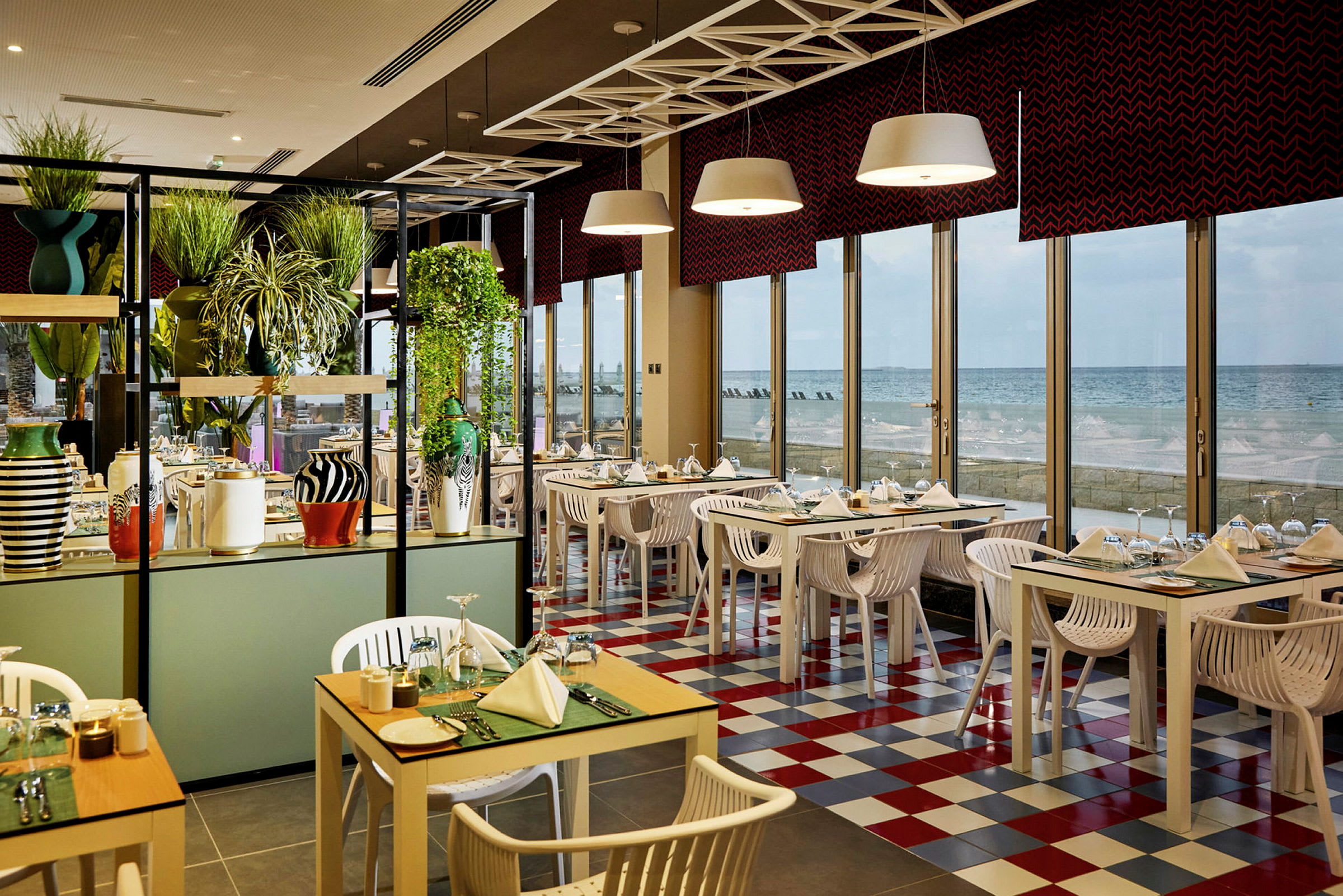 En restaurant med farverige borde og stole, store vinduer og udsigt over havet. (AI-genereret tekst)