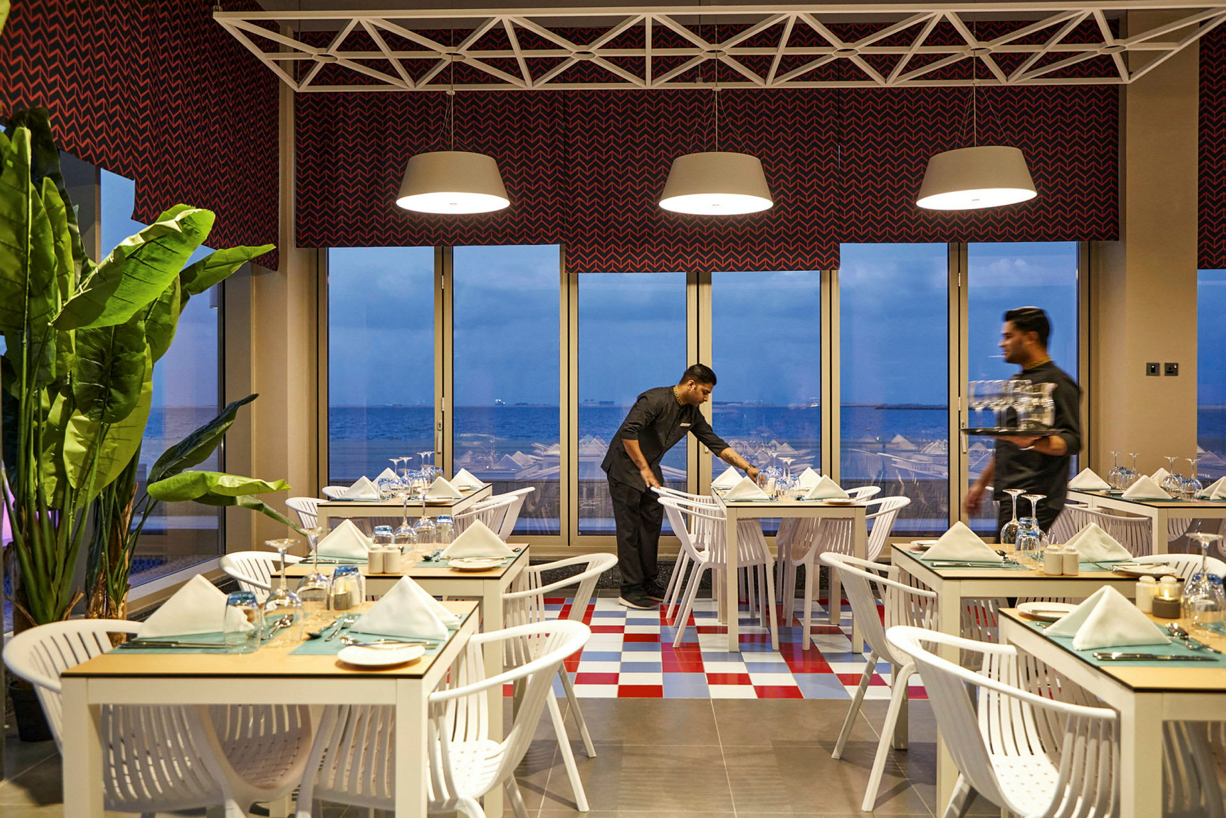 En lys restaurant med opdækkede borde og panoramaudsigt over havet gennem store vinduer. (AI-genereret tekst)