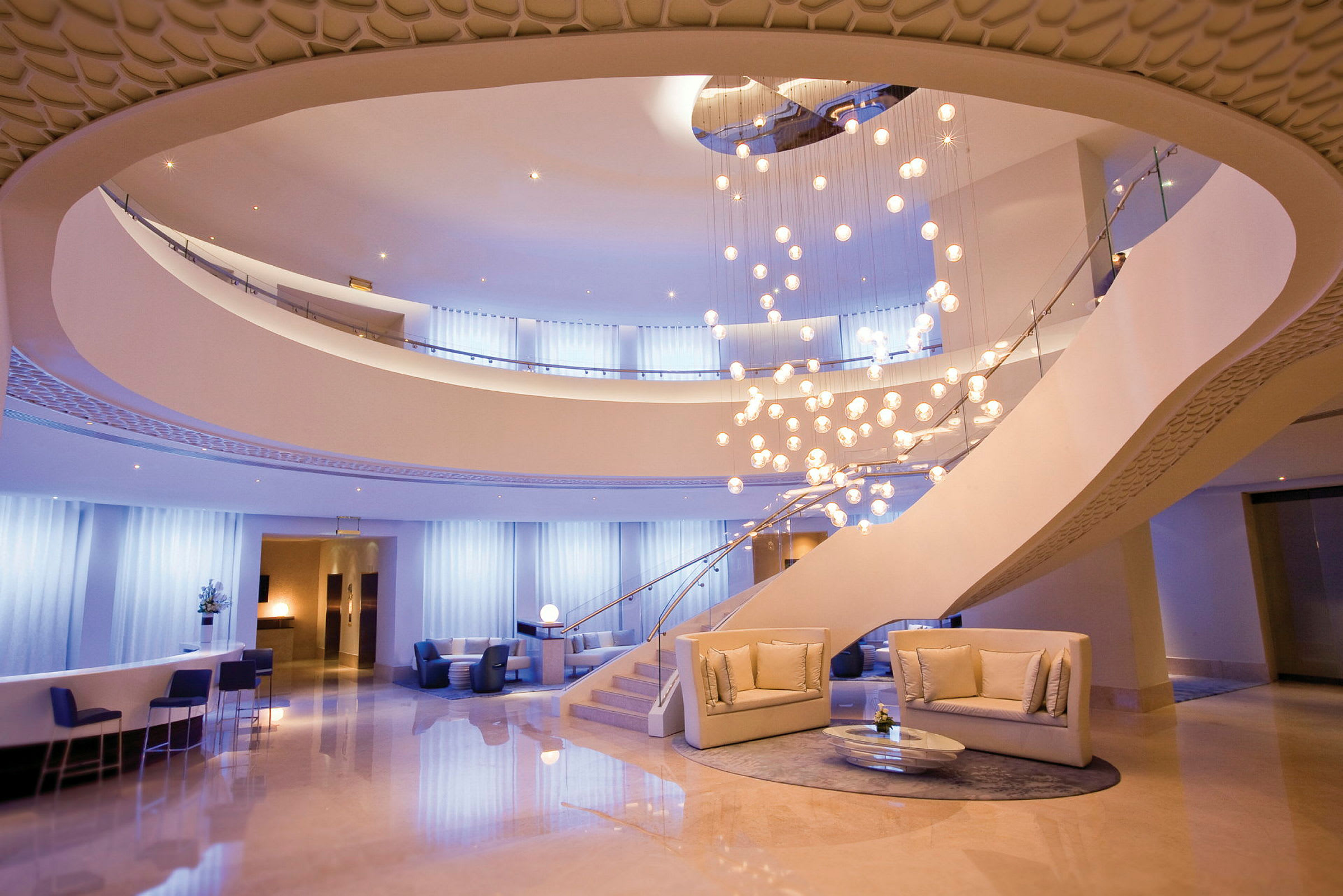 En elegant hotellobby med en stor lysekrone, moderne sofaer og et åbent niveau. (AI-genereret tekst)