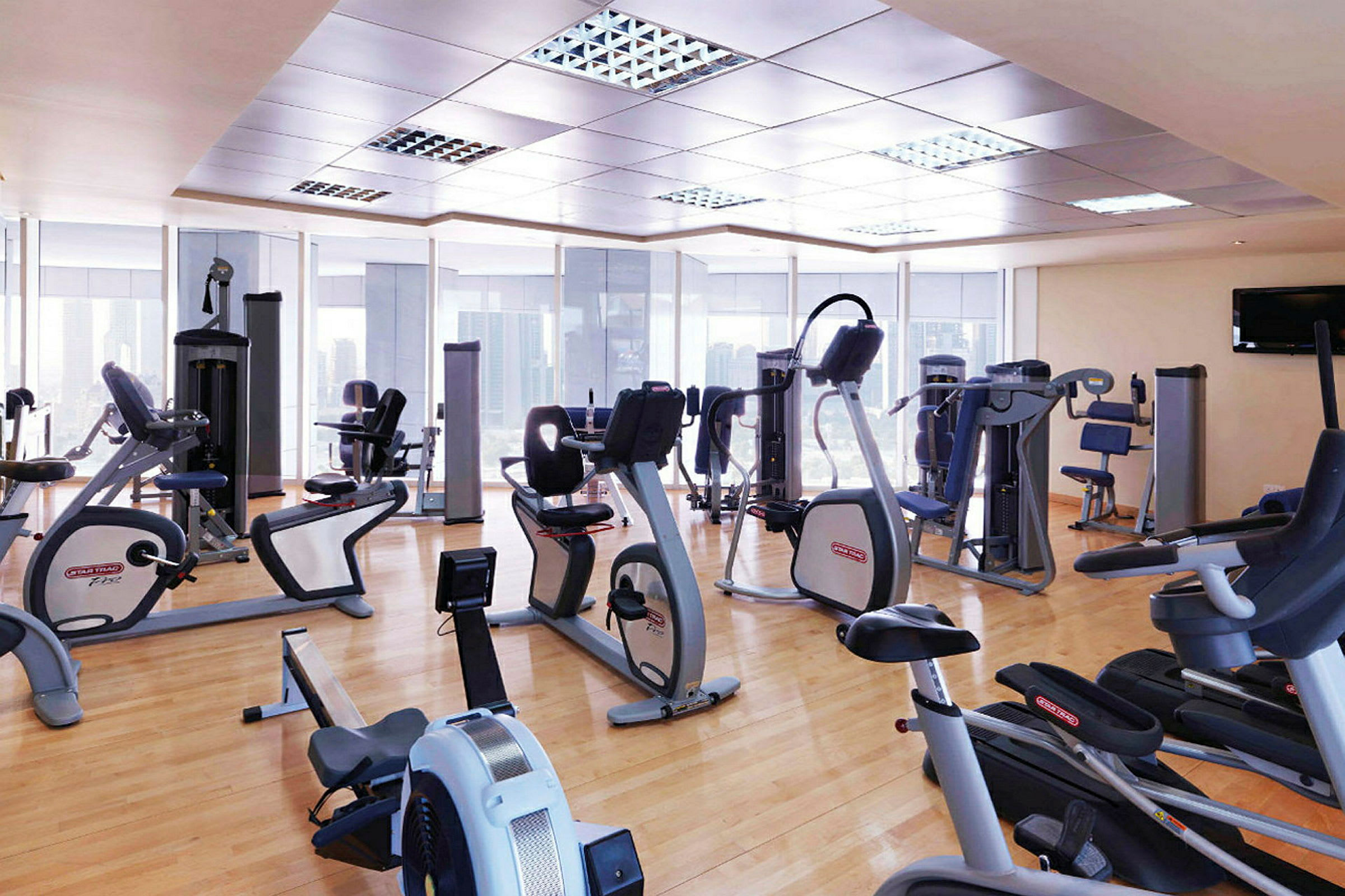 Fitnesscenter med forskellige træningsmaskiner og store glasvinduer. (AI-genereret tekst)