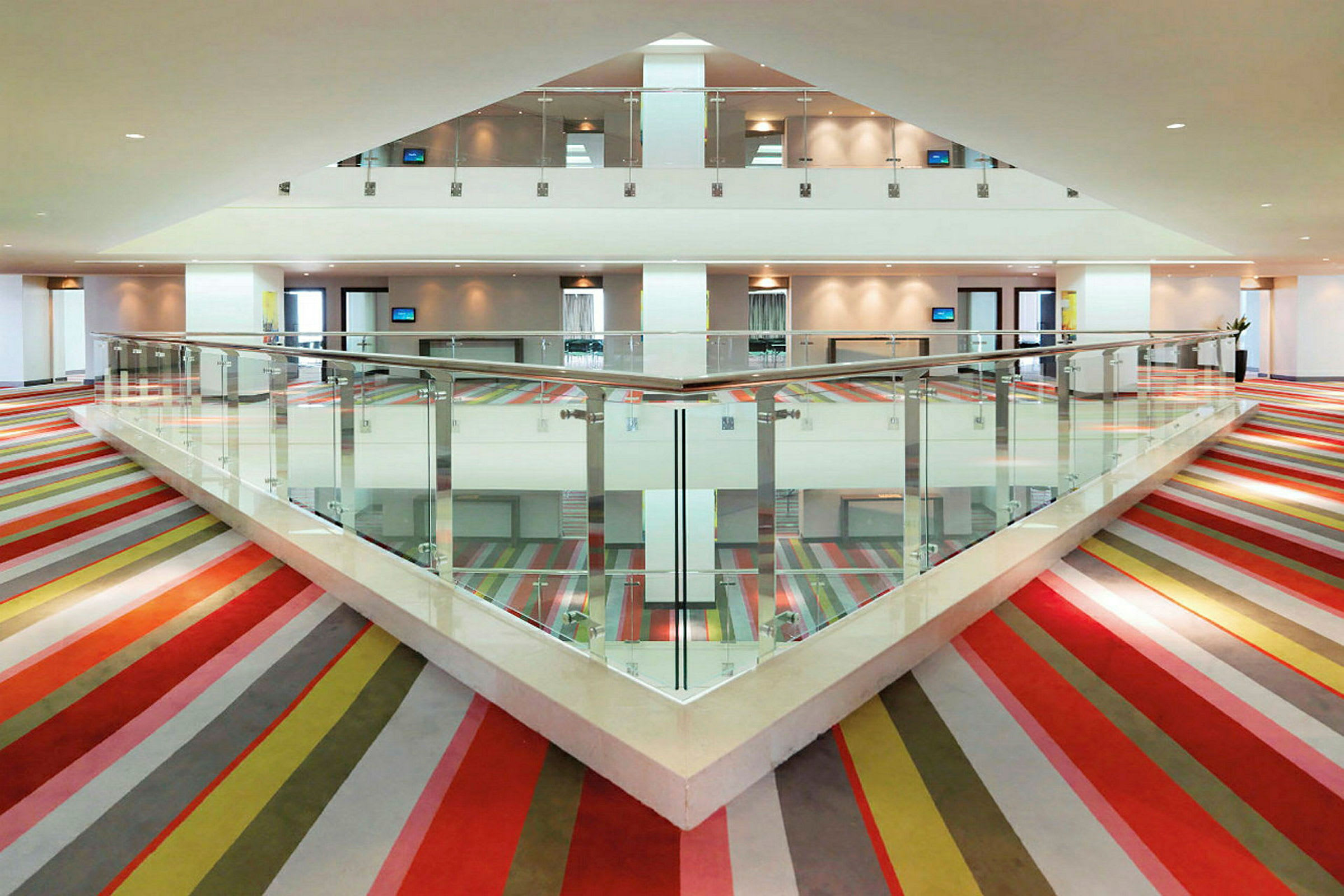 Interiør af en bygning med farverigt stribet tæppe og glasrækværk. (AI-genereret tekst)