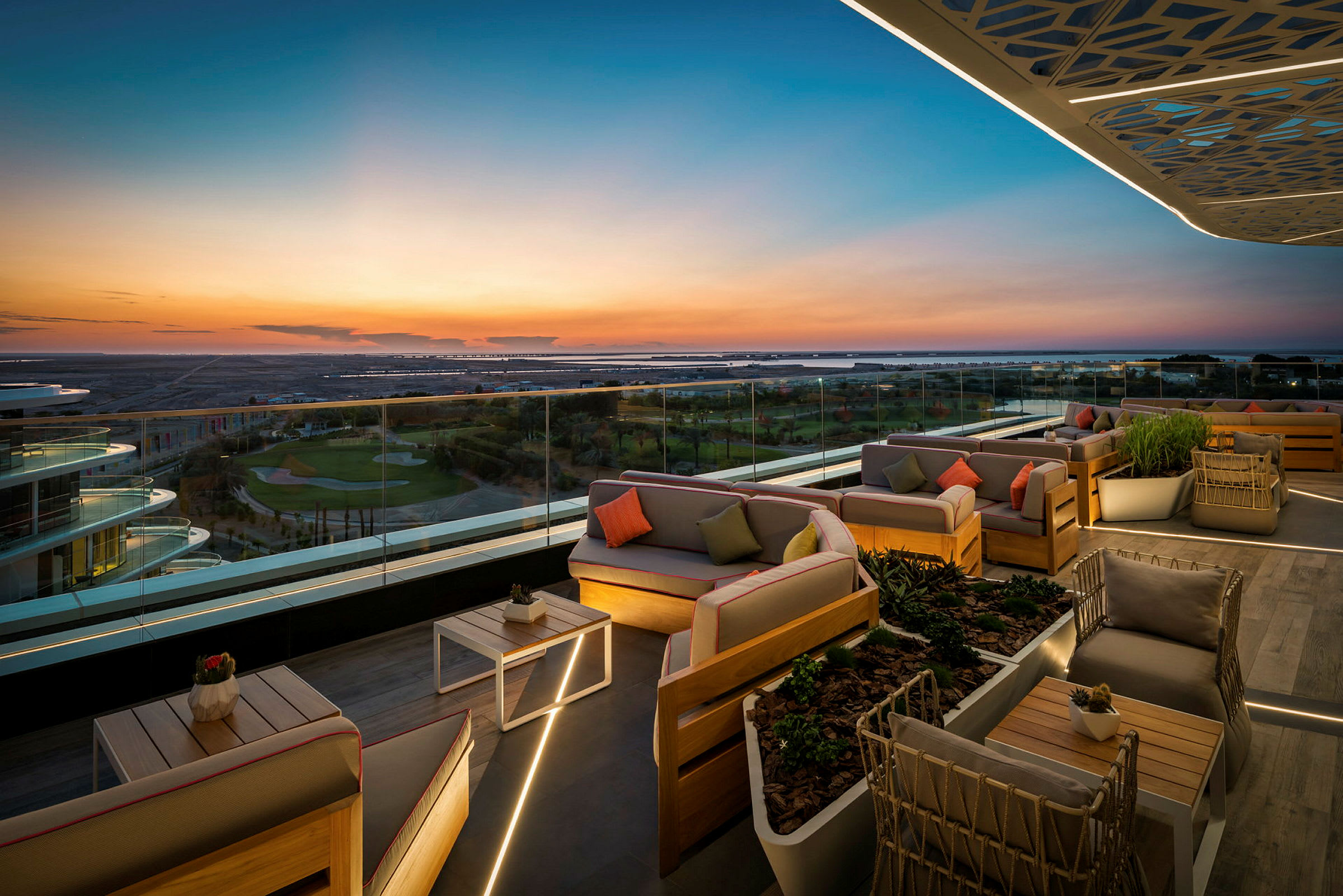 En tagterrasse med elegante siddeområder og glasrækværk, der giver panoramaudsigt over landskabet i solnedgang. (AI-genereret tekst)