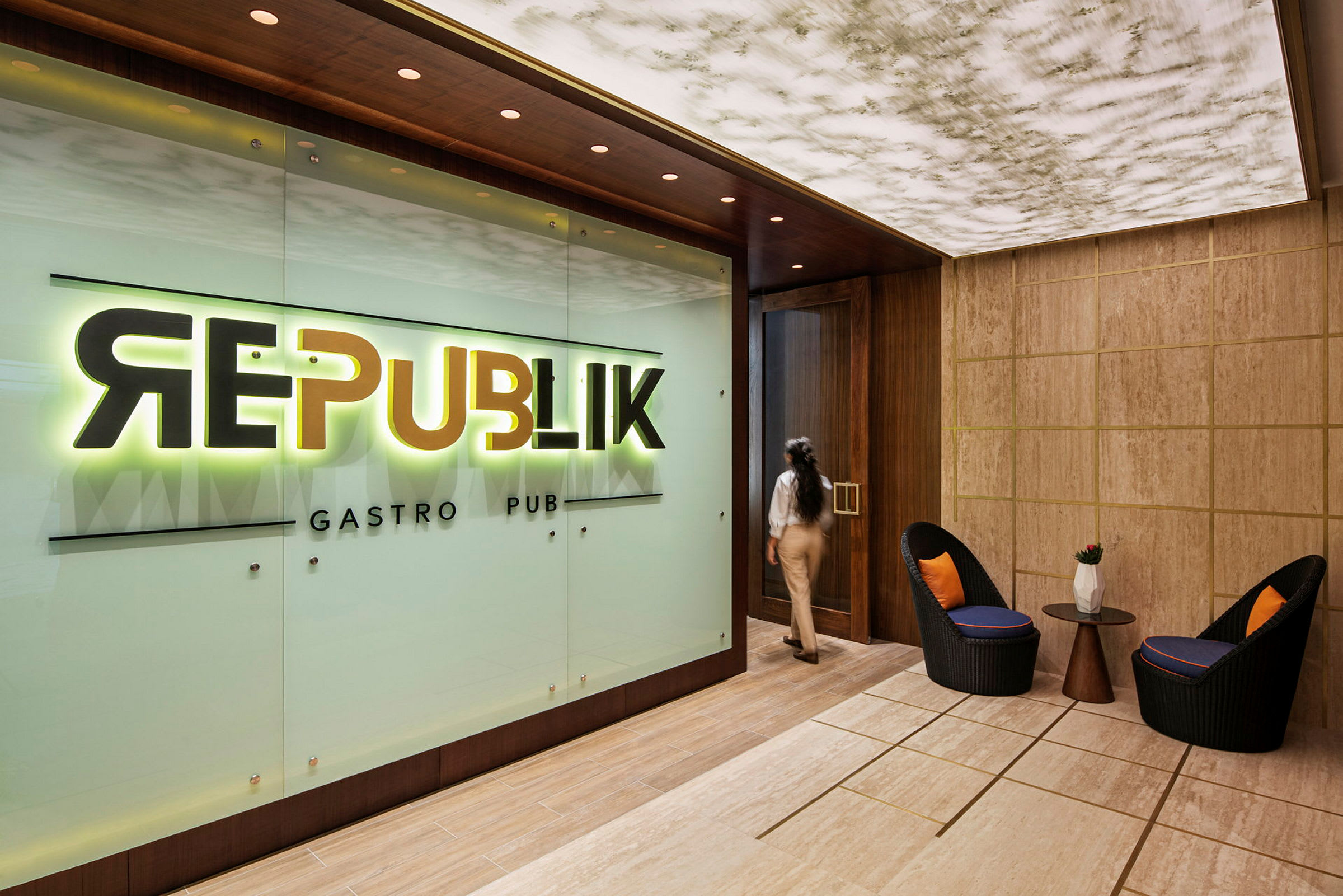 Indgangen til en restaurant eller bar med et skilt, der læser "Republik Gastro Pub". I forgrunden ses to stole og et bord. (AI-genereret tekst)