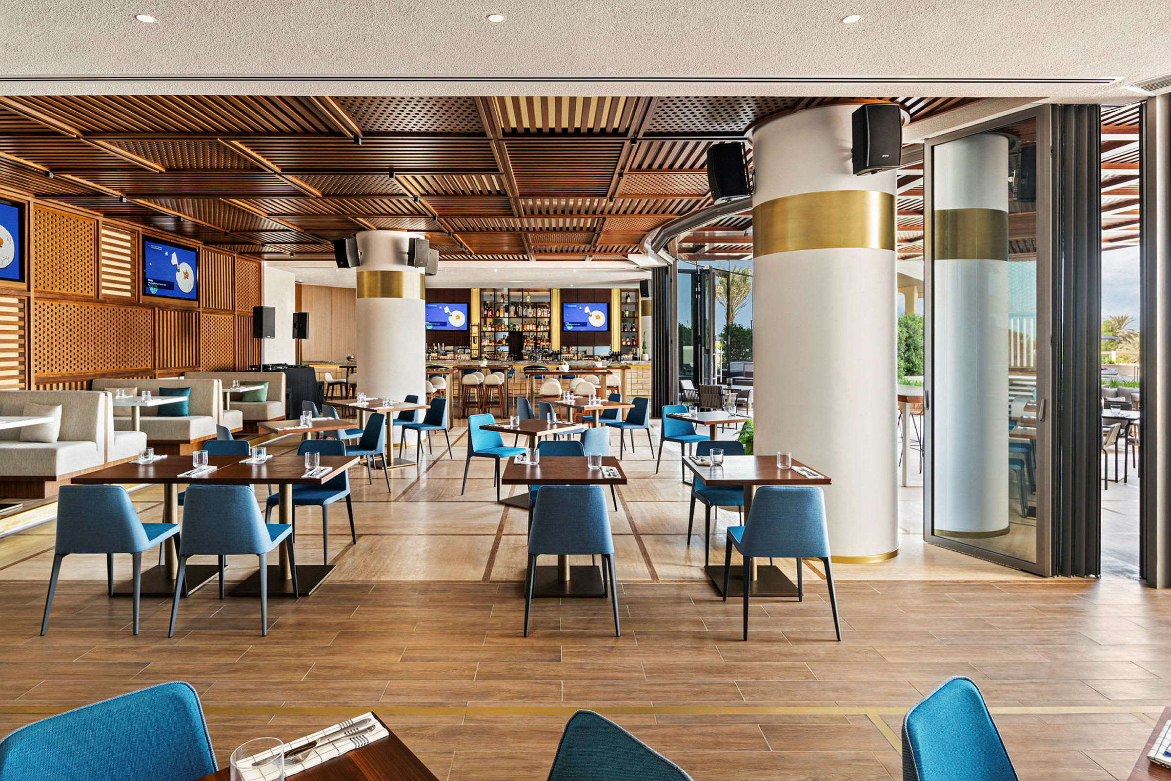 En moderne restaurant med træelementer i loftet, blå stole og dækkede borde. (AI-genereret tekst)
