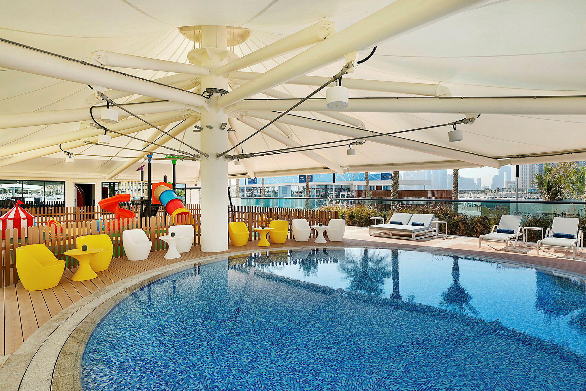 En udendørs swimmingpool omgivet af siddepladser og legeudstyr. (AI-genereret tekst)