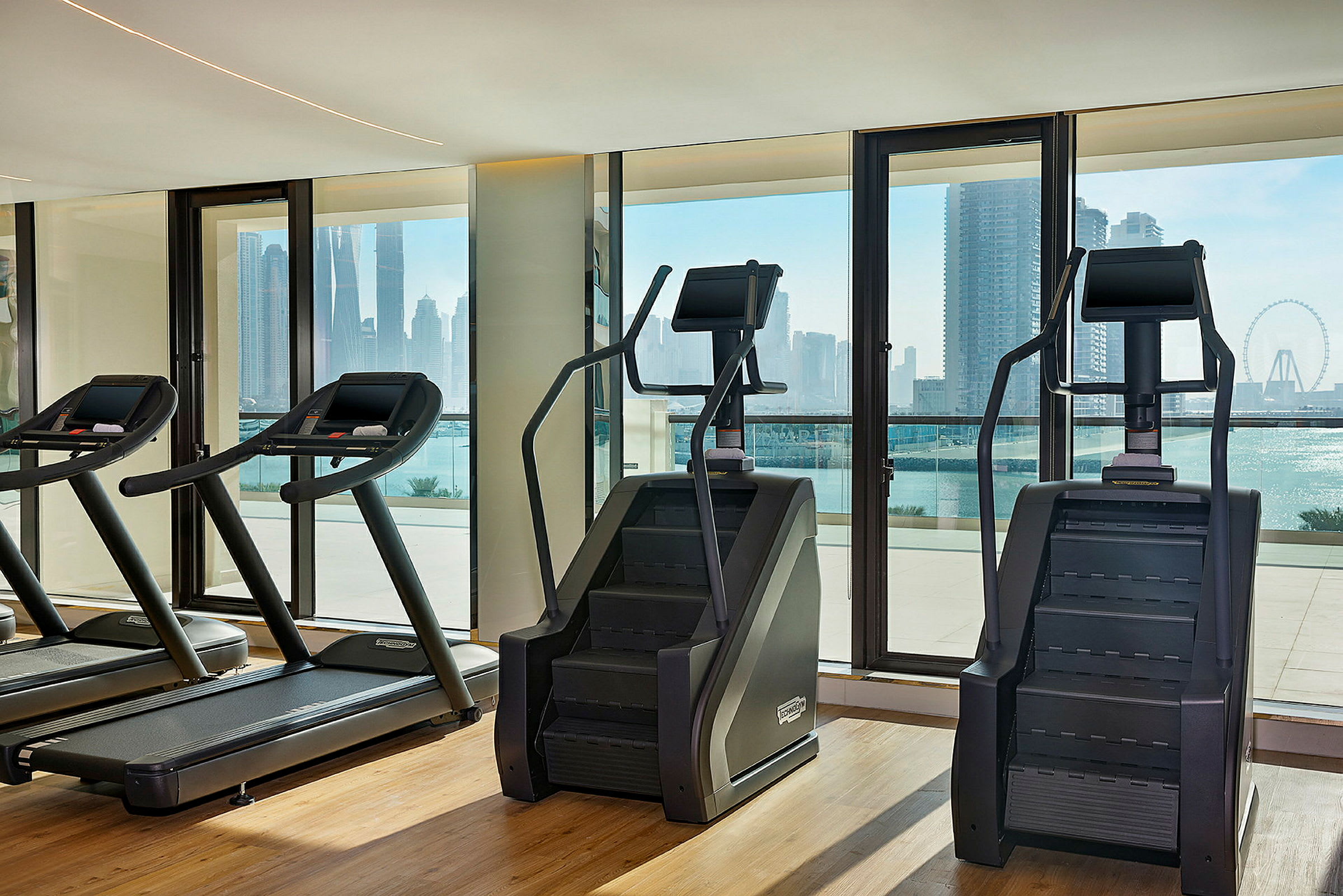 Træningsmaskiner i et fitnesscenter med udsigt til en byens silhuet. (AI-genereret tekst)
