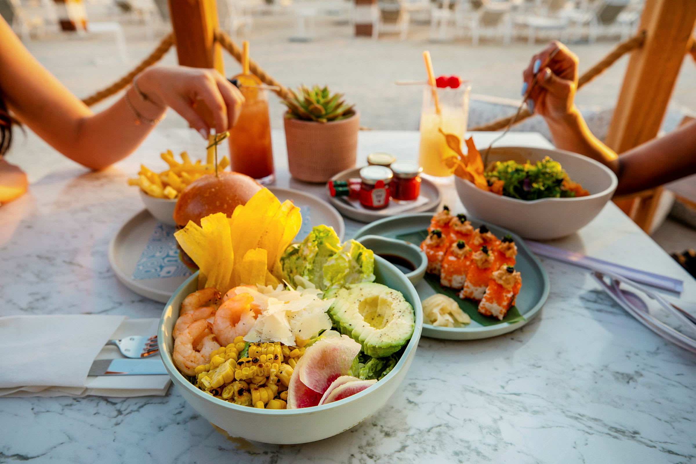 Et bord fyldt med forskellige retter, herunder salat, sushi, burger og drikkevarer. (AI-genereret tekst)