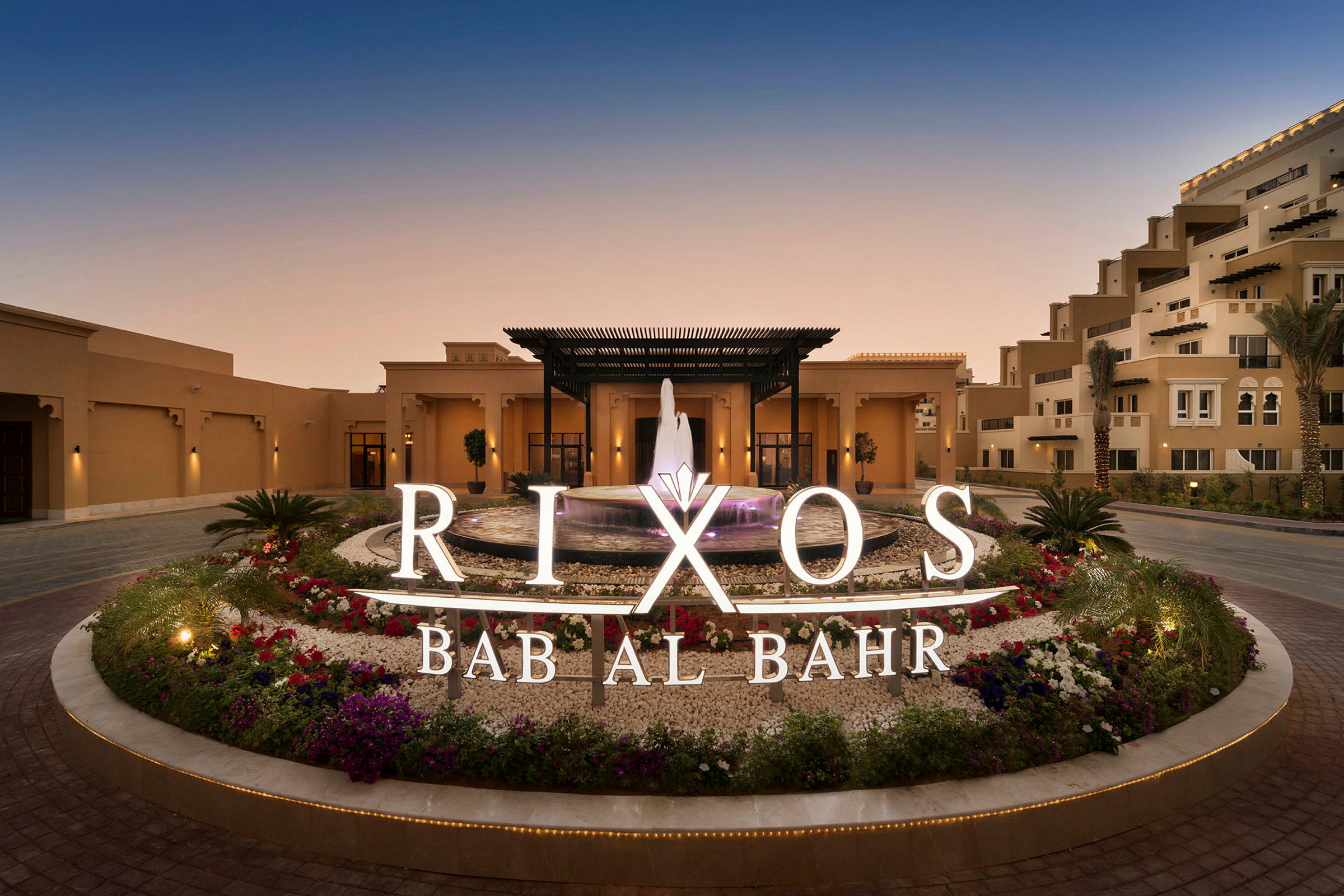 Hotelindgang med springvand og omkringliggende blomster, skilt med teksten Rixos Bab Al Bahr. (AI-genereret tekst)