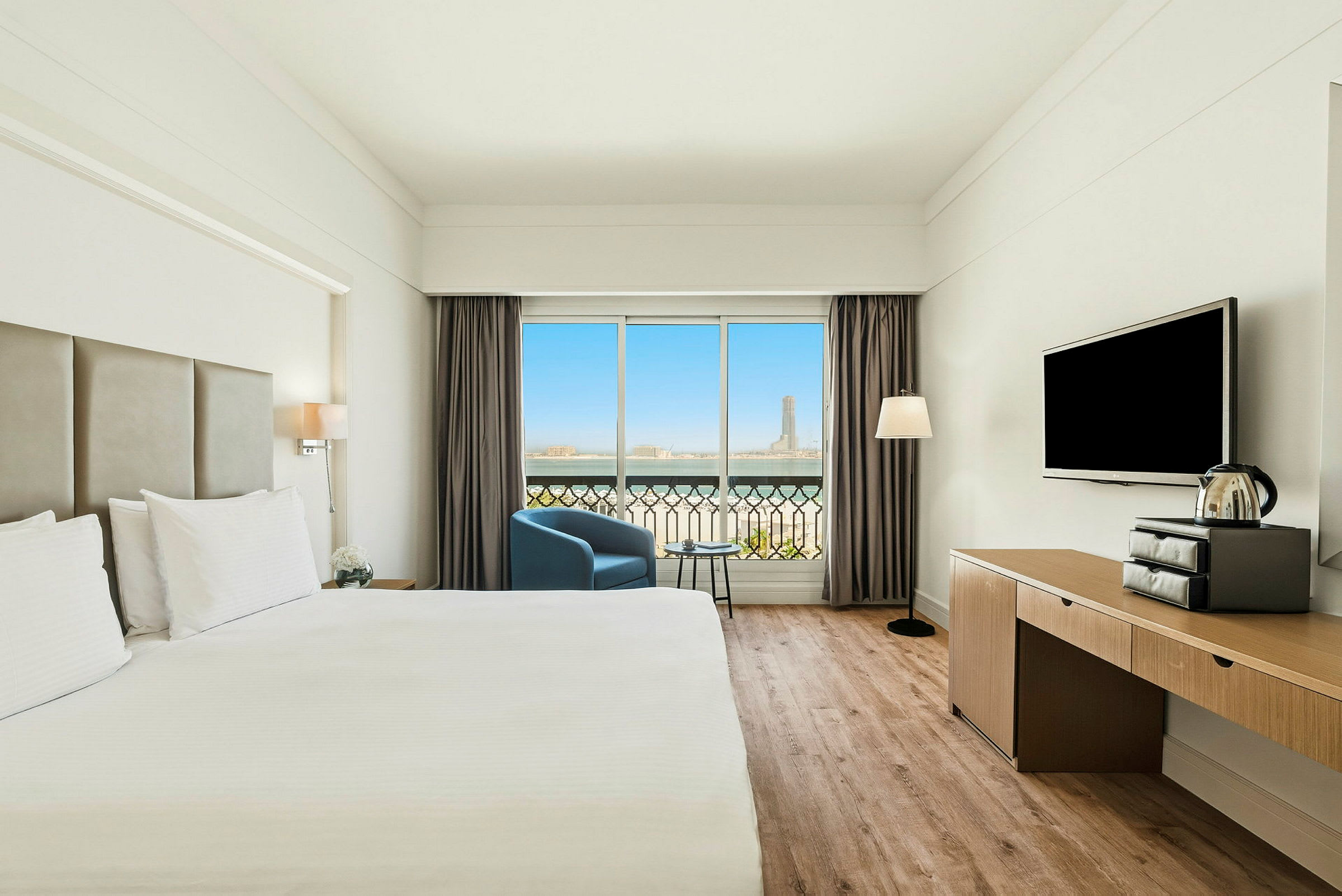 Et moderne hotelværelse med en stor seng, et fjernsyn, en lænestol og et vindue med udsigt. (AI-genereret tekst)