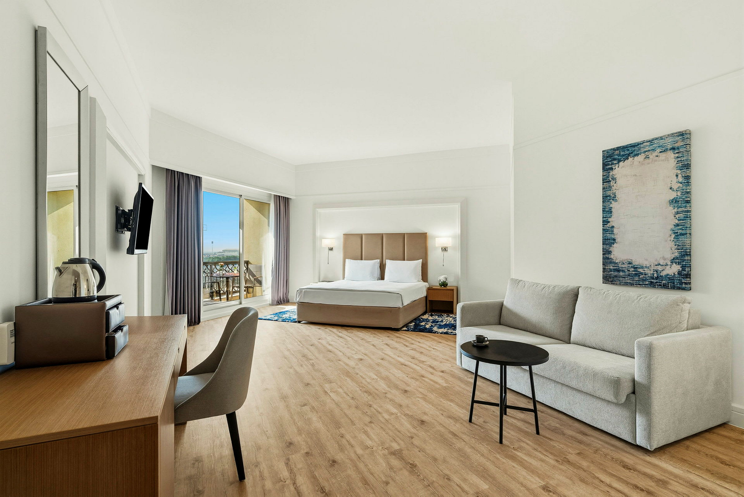 Hotelværelse med en dobbeltseng, en sofa og et skrivebord samt en balkon med udsigt. (AI-genereret tekst)