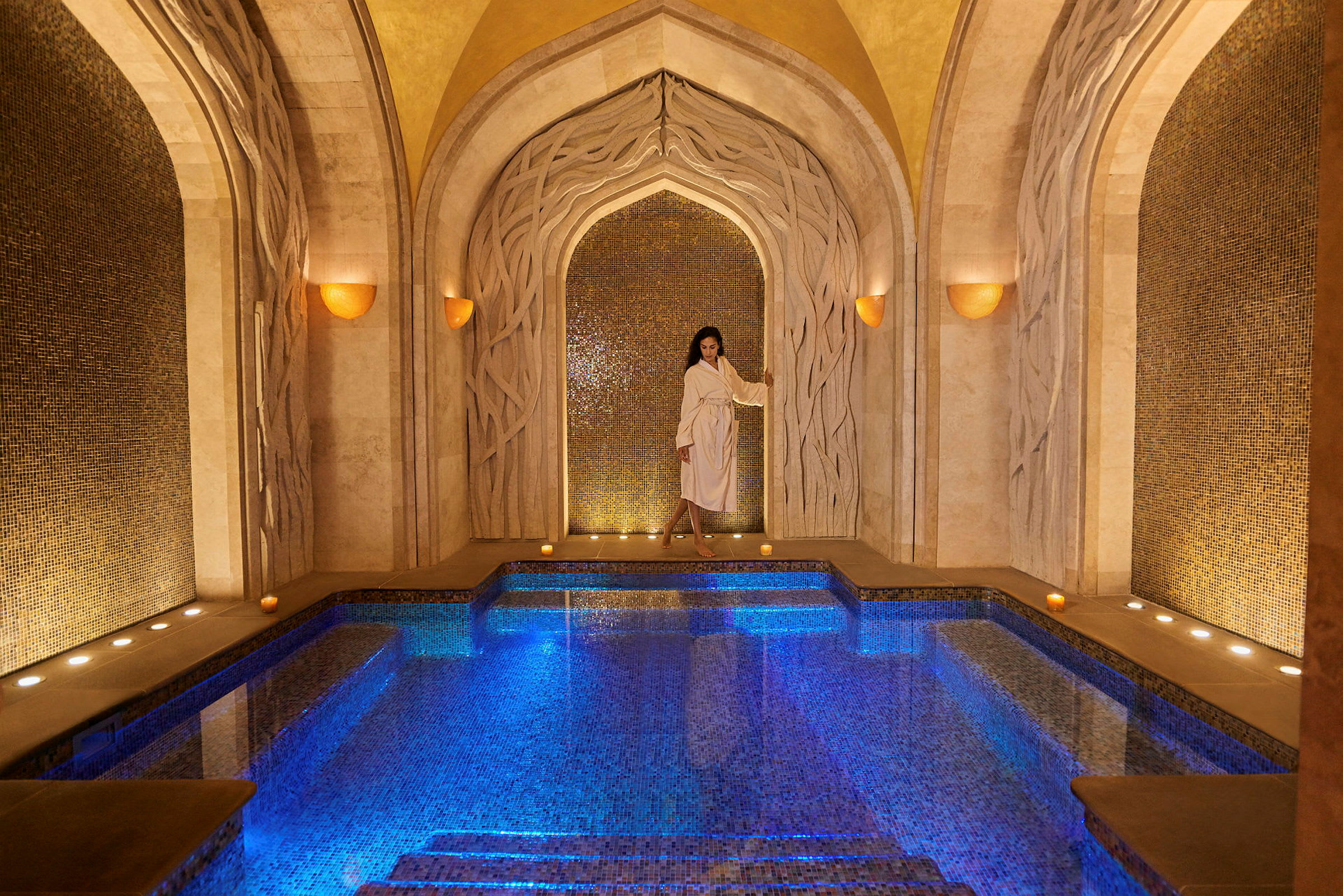 Elegant spa-miljø med oplyst mosaikpool og dekorative hvælvinger. (AI-genereret tekst)