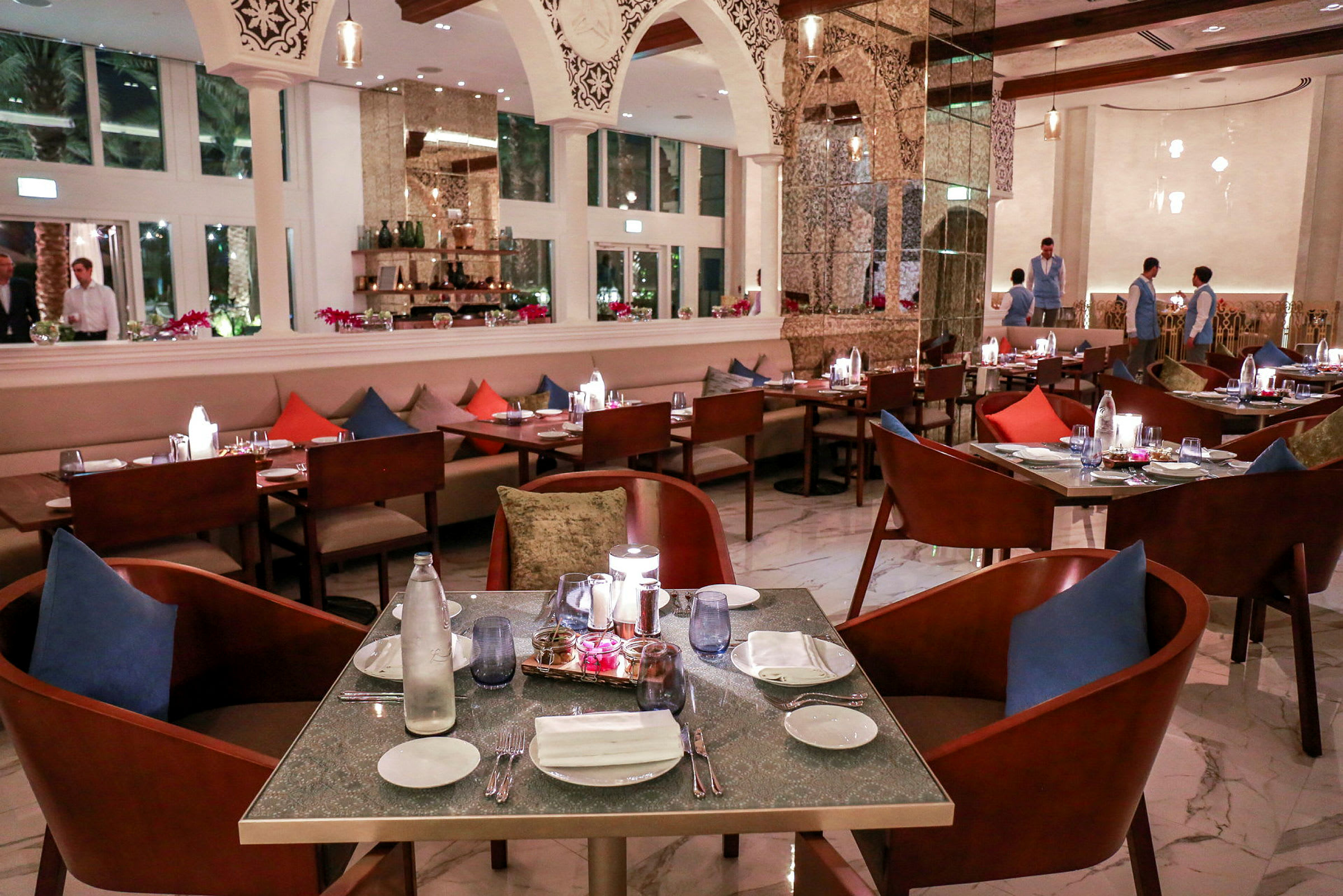 En elegant restaurant med dækket bord, farvede puder og moderne interiørdetaljer. (AI-genereret tekst)