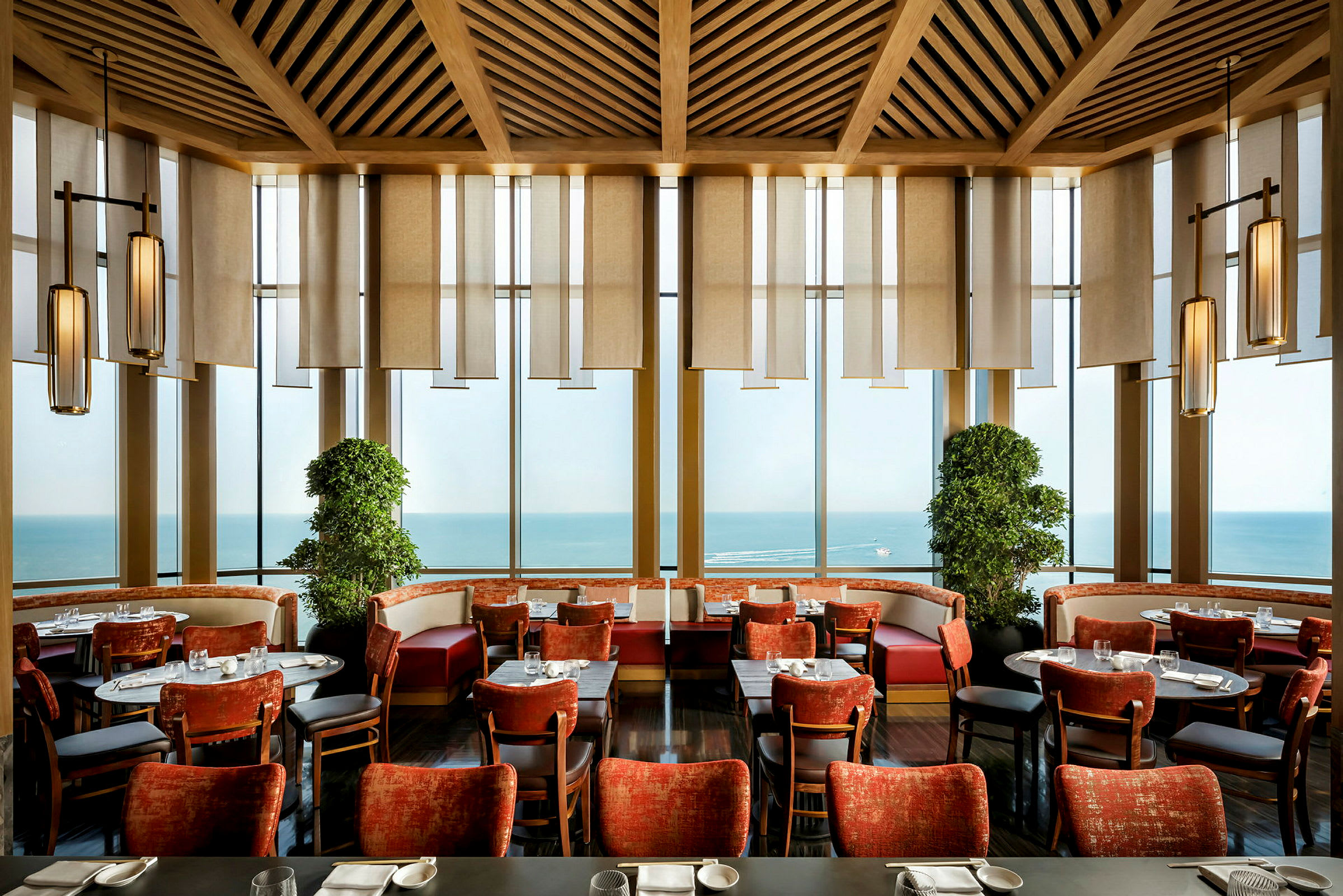 Interiør af en restaurant med røde stole, panoramavinduer og havudsigt. (AI-genereret tekst)