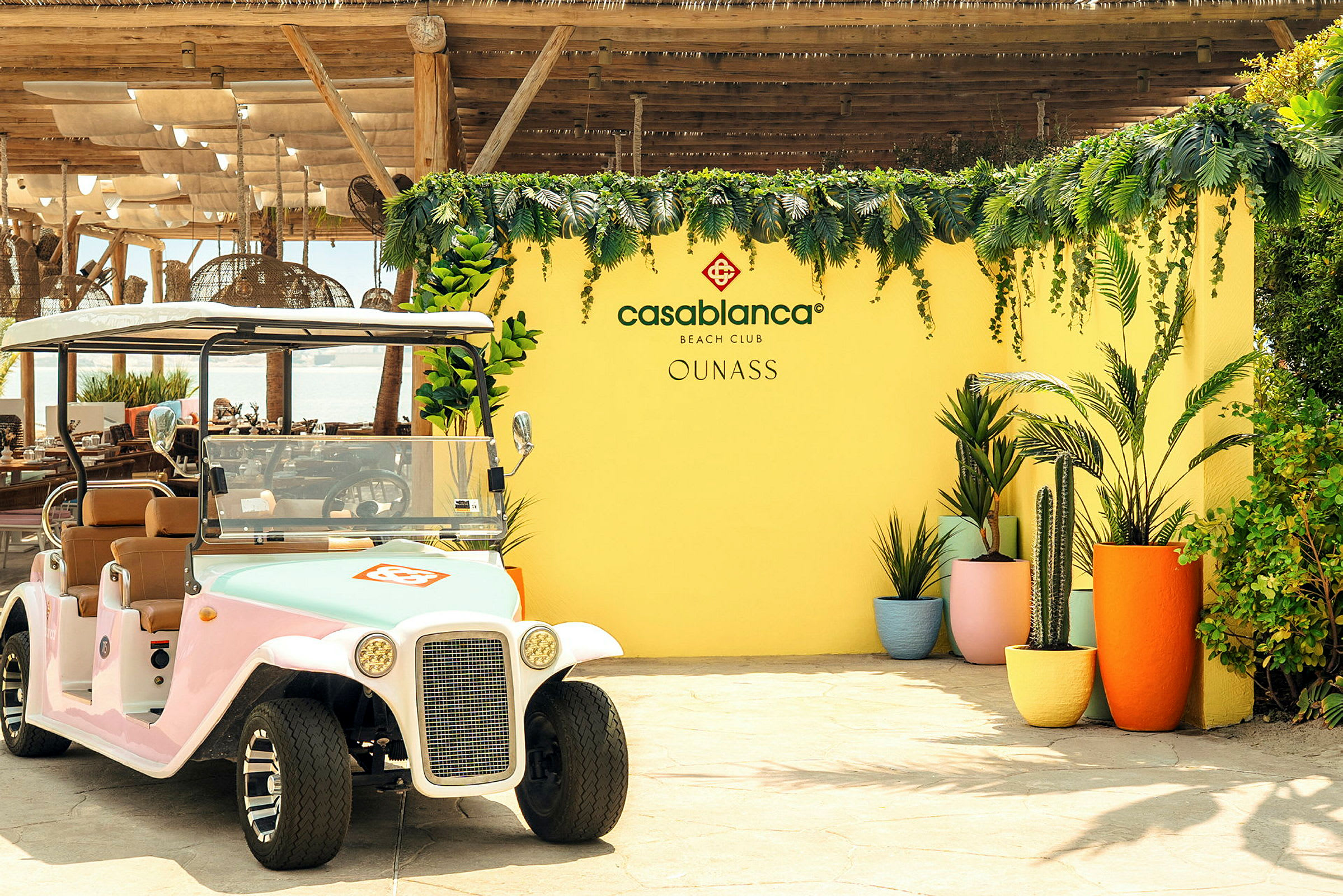 En golfbil står foran en gul væg dekoreret med vegetation og blomster samt teksten 'Casablanca Beach Club'. (AI-genereret tekst)