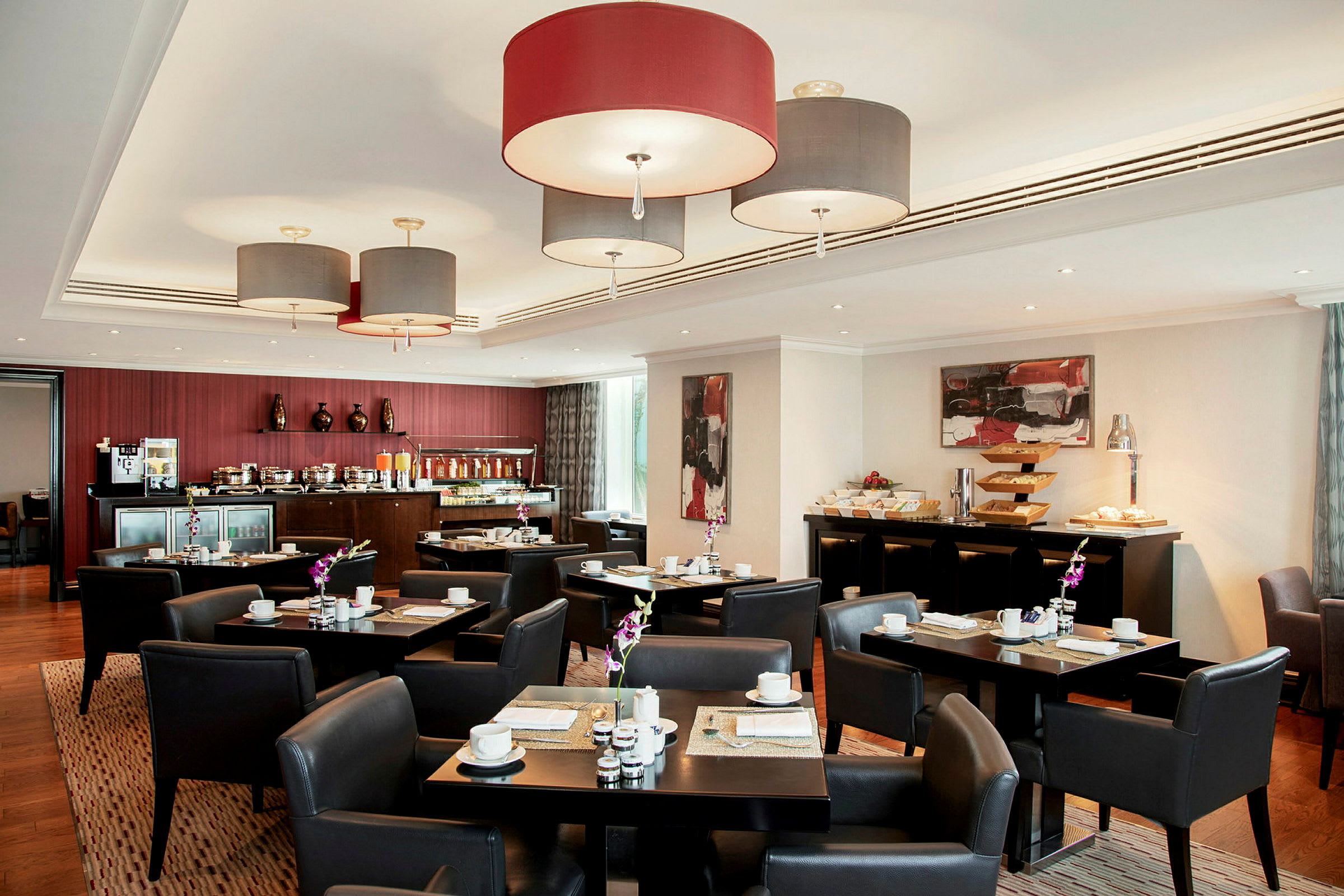 Et bistroområde med borde og stole omgivet af en buffetservering. Hængende lamper og kunst på væggene fuldender interiøret. (AI-genereret tekst)