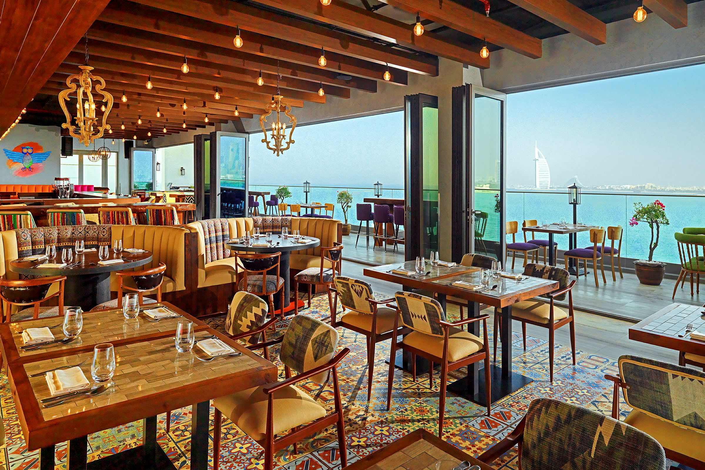 Restaurant med moderne møbler, farverigt flisegulv og panoramaudsigt over havet. (AI-genereret tekst)