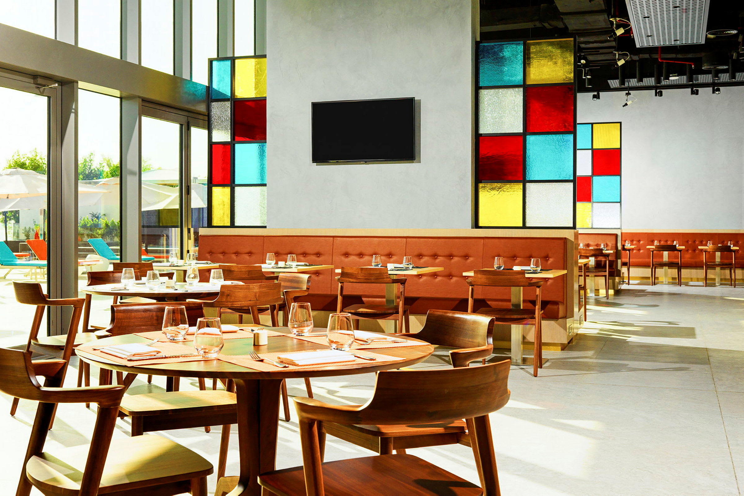 Billede af en moderne restaurant med farverige glaspaneler og træborde, dækket op til gæster. (AI-genereret tekst)