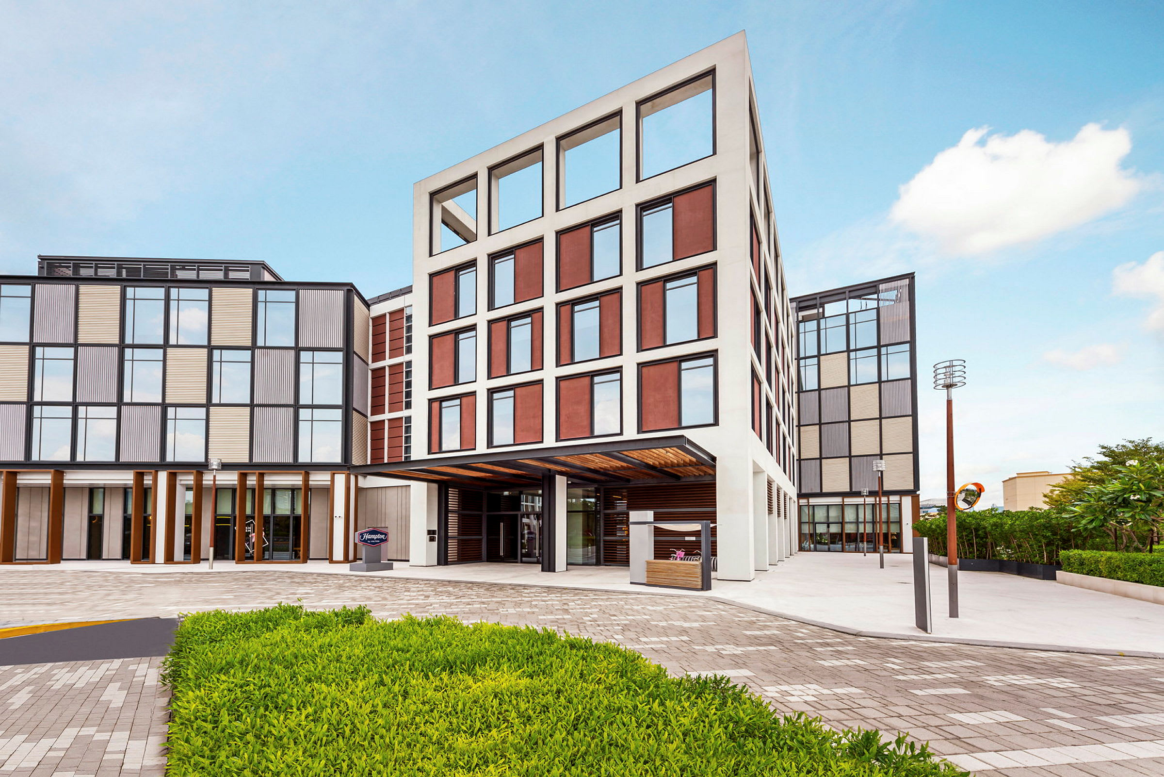 En moderne bygning med store vinduer og farvede paneler. Foran bygningen er der en grusvej og en græsplæne. (AI-genereret tekst)