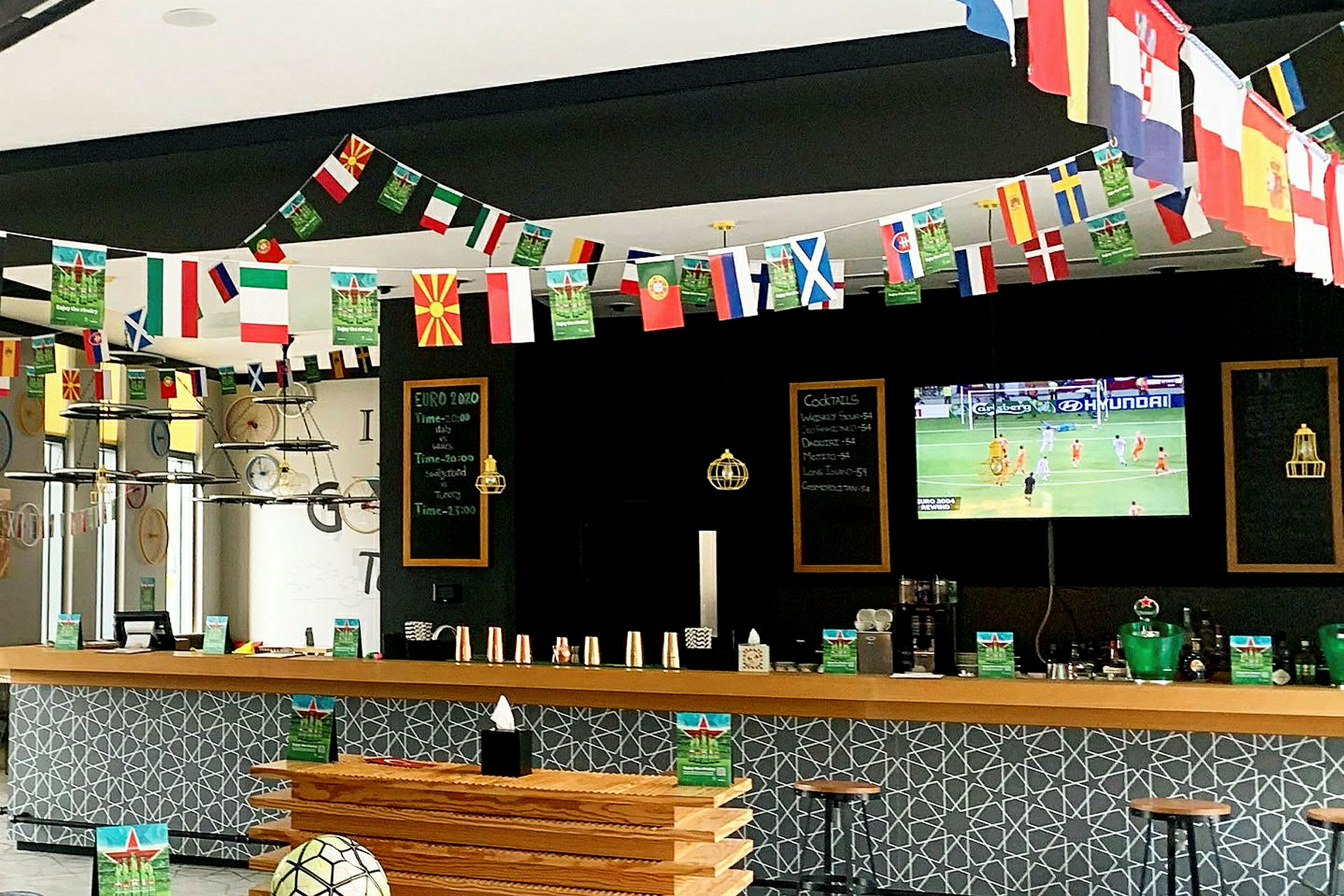 En sportsbar med dekorationer af landsflag og et fjernsyn, der viser en fodboldkamp. (AI-genereret tekst)