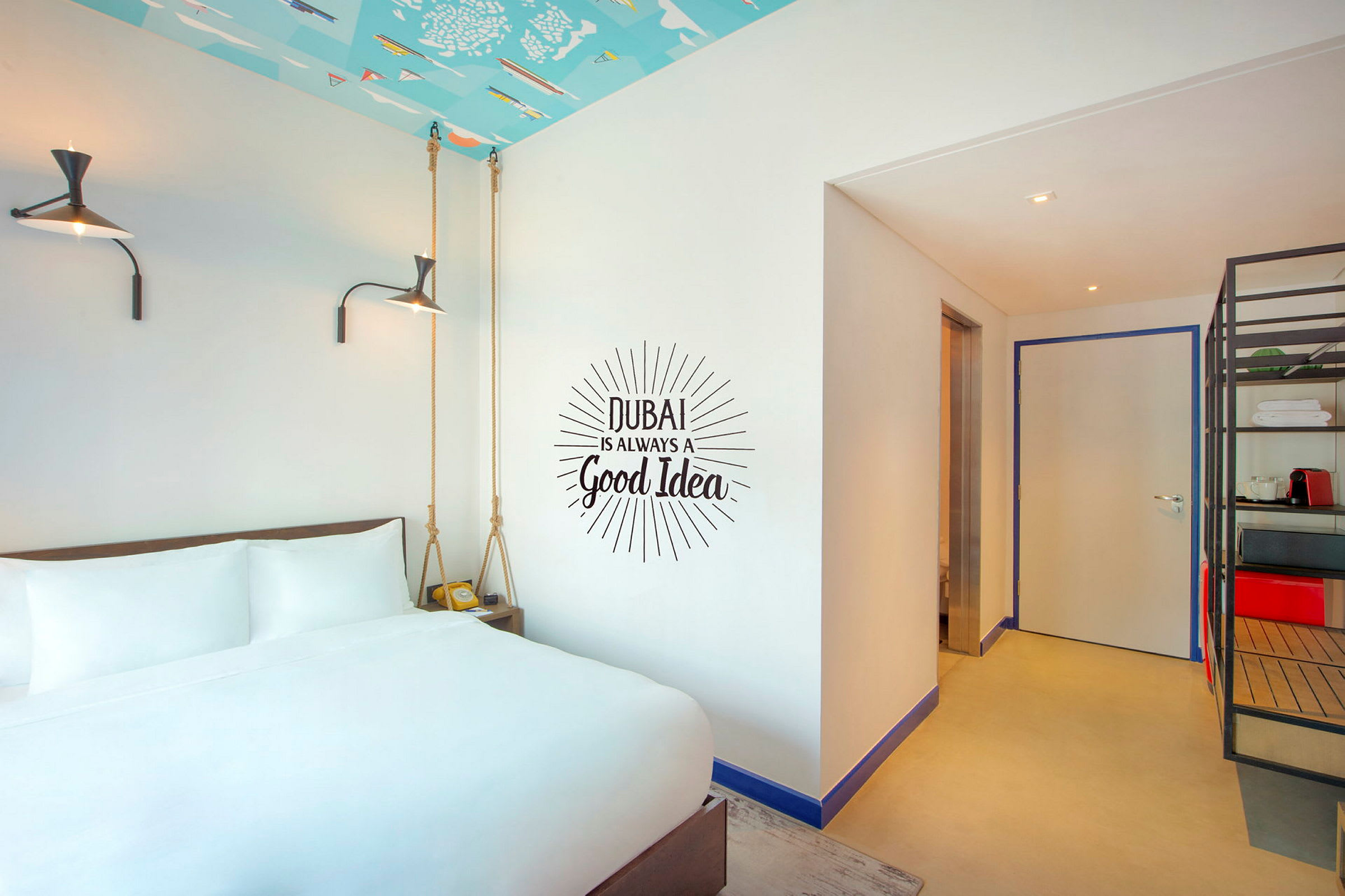 Hotelværelse med hvid seng foran en væg med teksten "Dubai is always a good idea". (AI-genereret tekst)