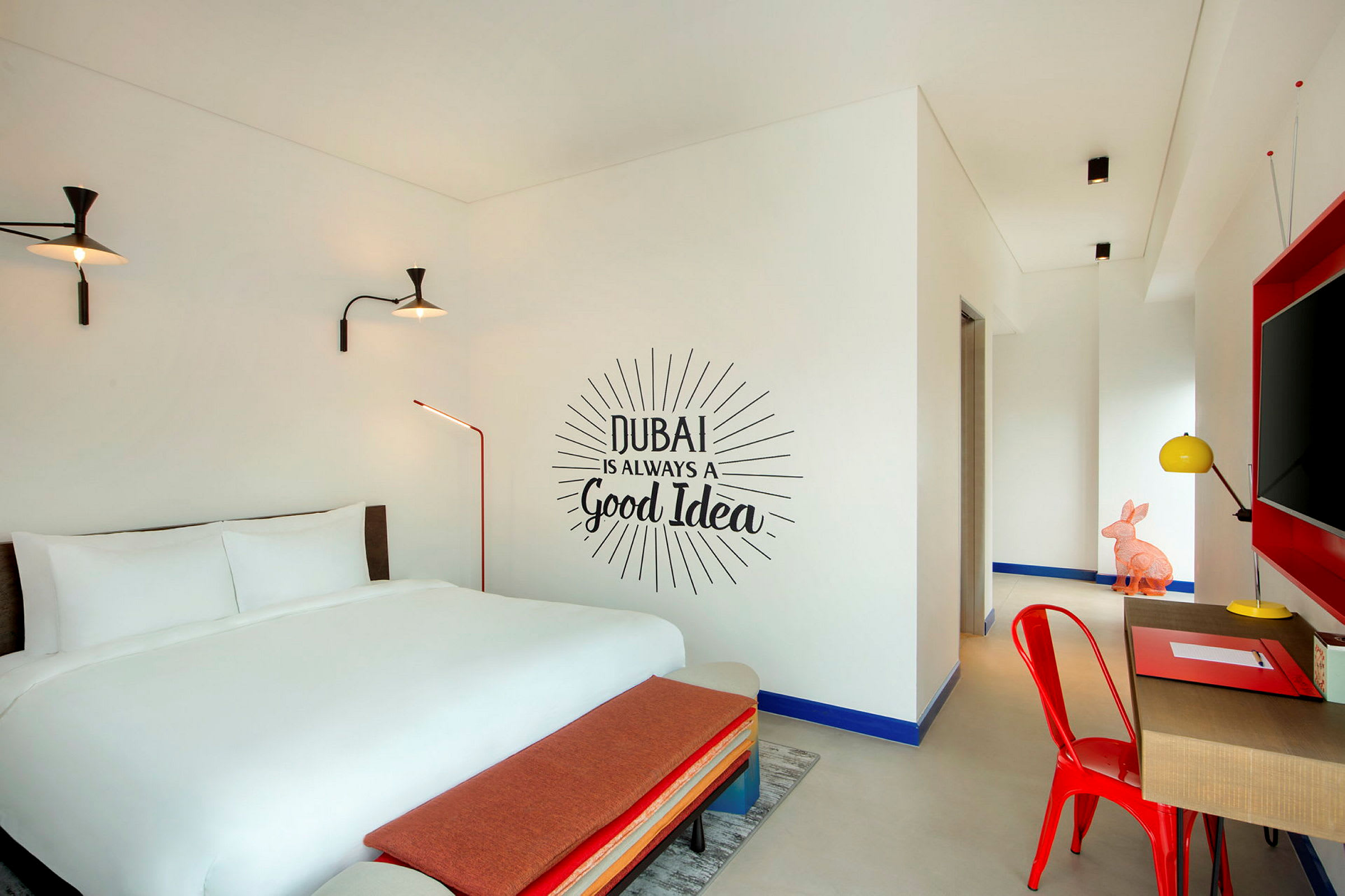 Et hotelværelse med en dobbeltseng, en vægtekst der lyder "Dubai is always a good idea", og indretning i moderne farver. (AI-genereret tekst)