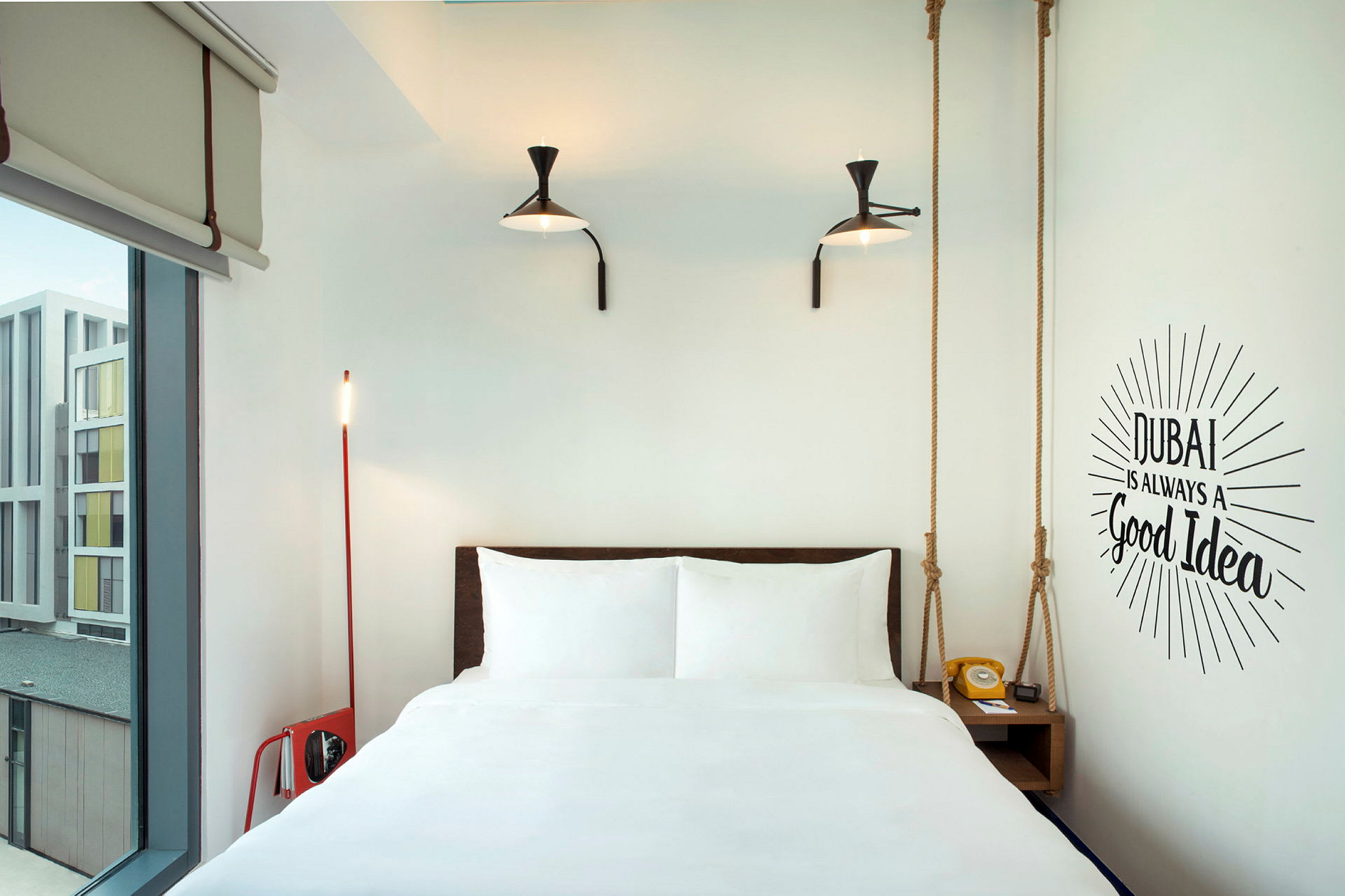 Et moderne hotelværelse med en seng, to lamper på væggen og en vægtekst, der lyder "Dubai is always a good idea". (AI-genereret tekst)