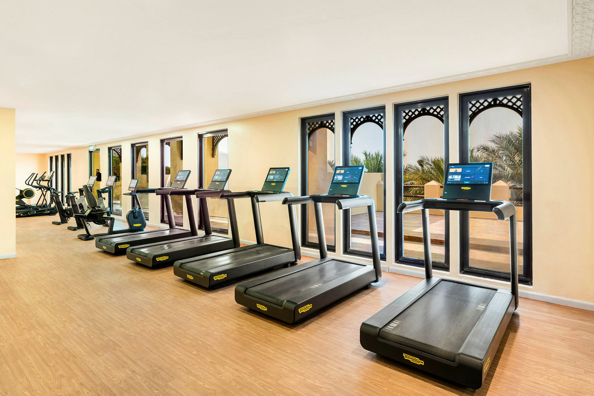 Et fitnesscenter med løbebånd og træningsmaskiner foran vinduer. (AI-genereret tekst)