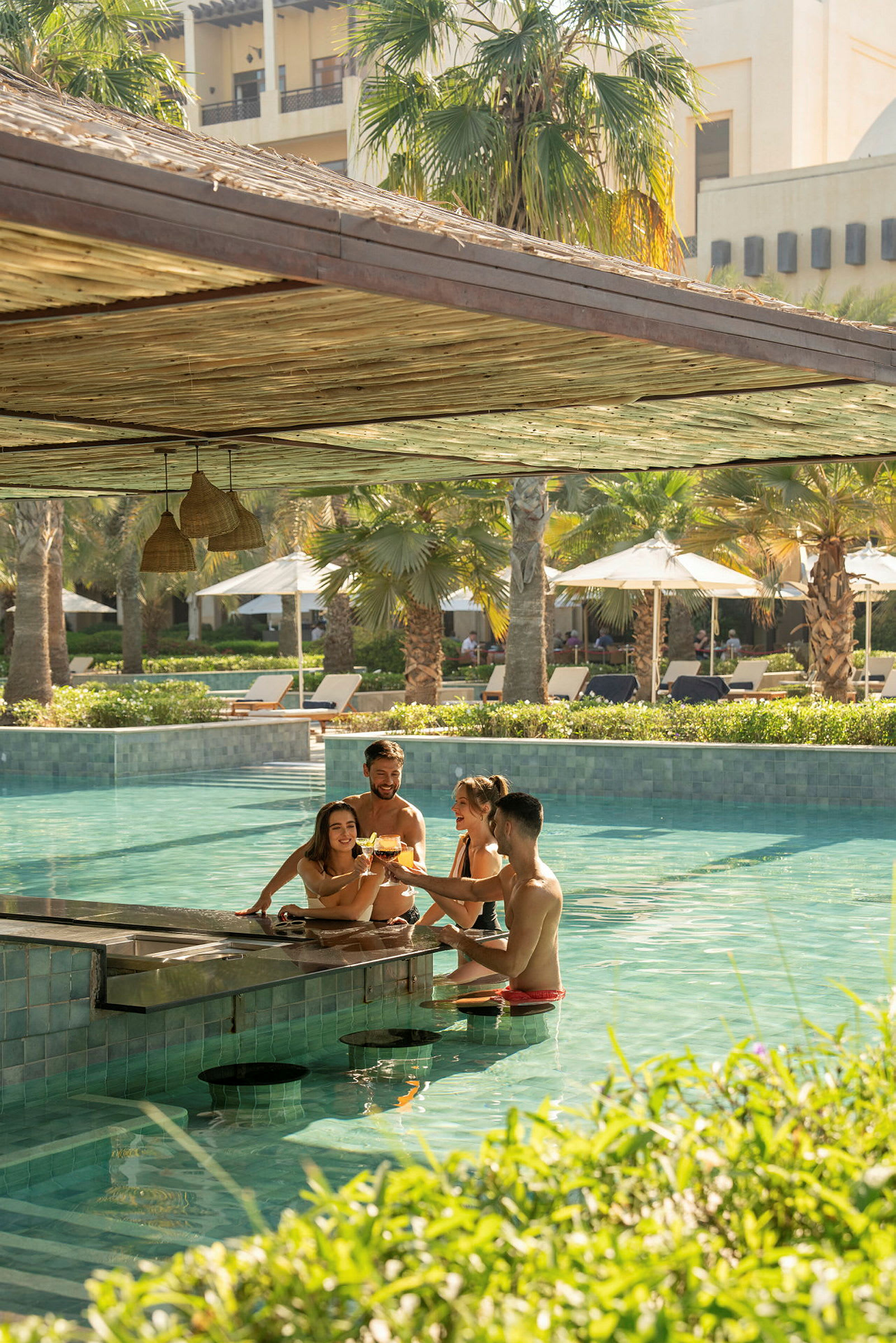 En poolbar, hvor folk nyder drinks, mens de sidder i vandet, omgivet af solsenge og palmer. (AI-genereret tekst)