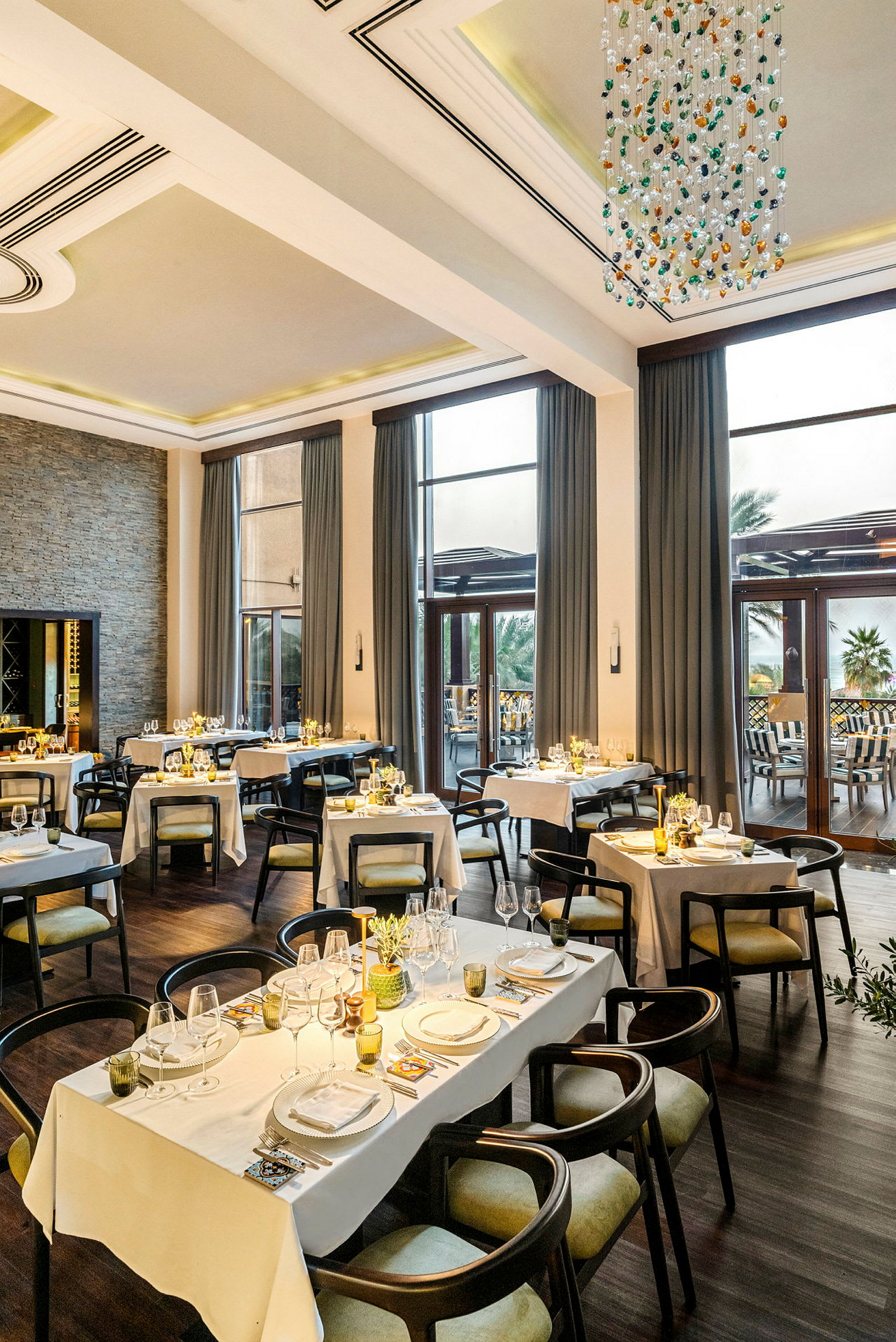 En elegant restaurant med opdækkede borde til middag, store vinduer og en lysekrone i loftet. (AI-genereret tekst)