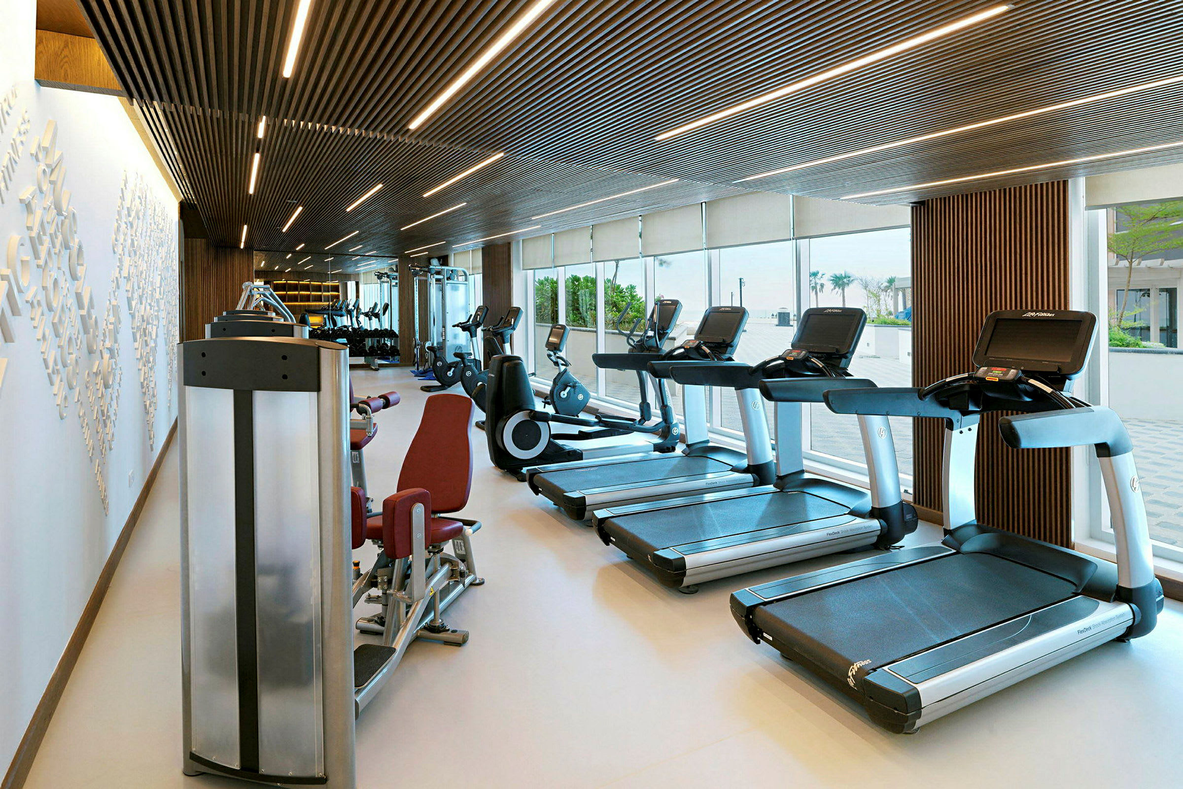 Et moderne fitnesscenter med træningsudstyr som løbebånd og motionscykler, med store vinduer, der lukker dagslys ind. (AI-genereret tekst)