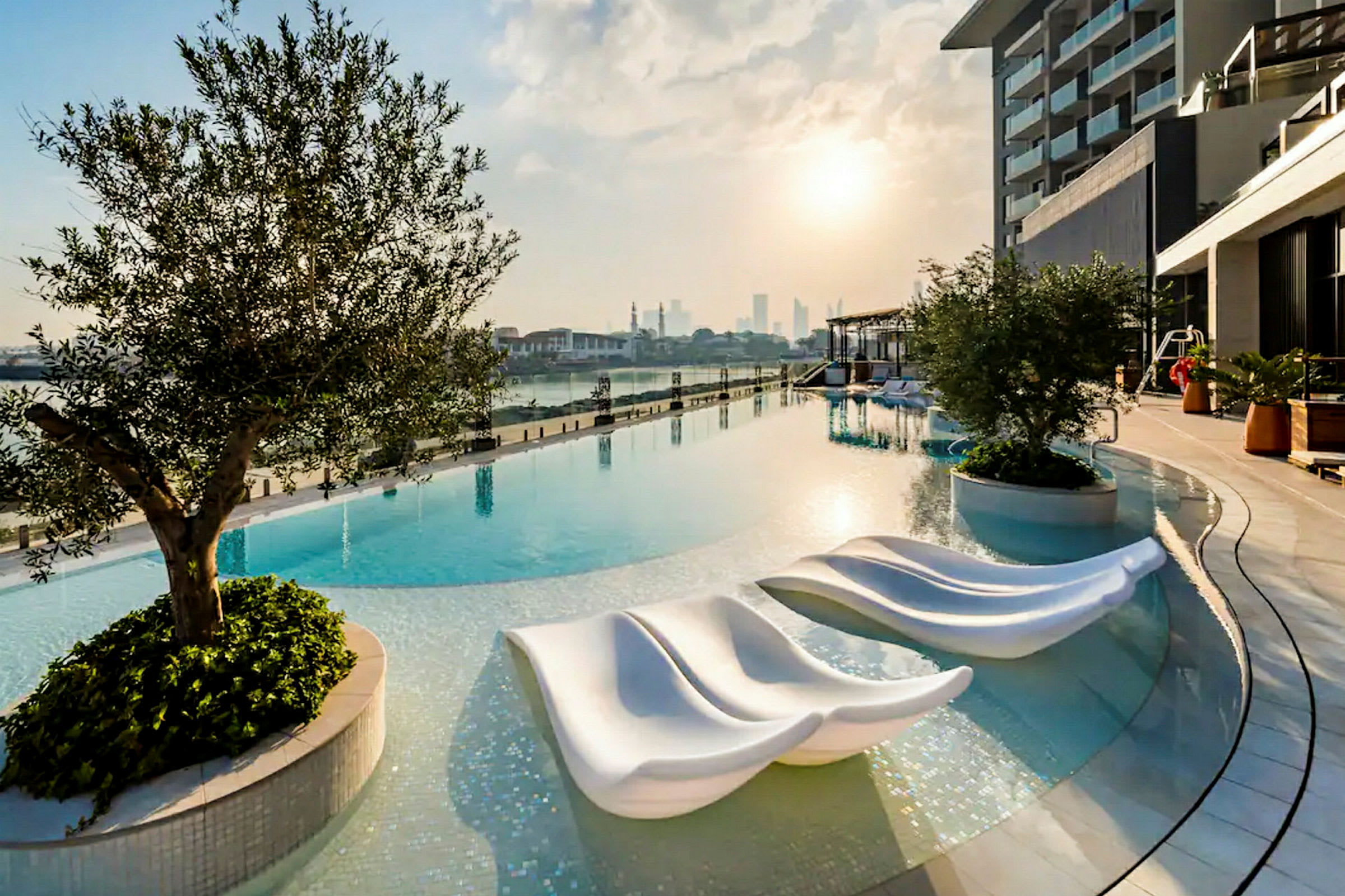 Billede af en infinitypool ved solnedgang med moderne solsenge og omgivelser med beplantning. (AI-genereret tekst)