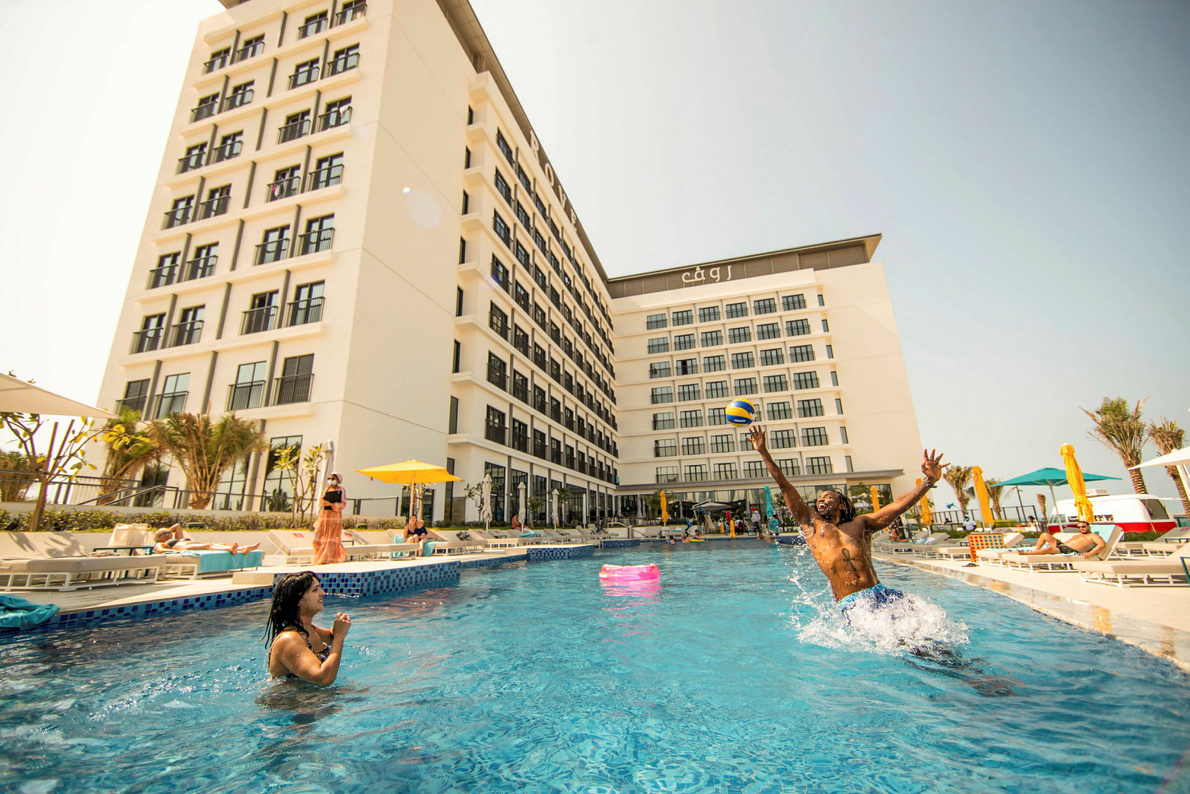 Et hotel med hvid facade, omgivet af en pool og liggestole. (AI-genereret tekst)