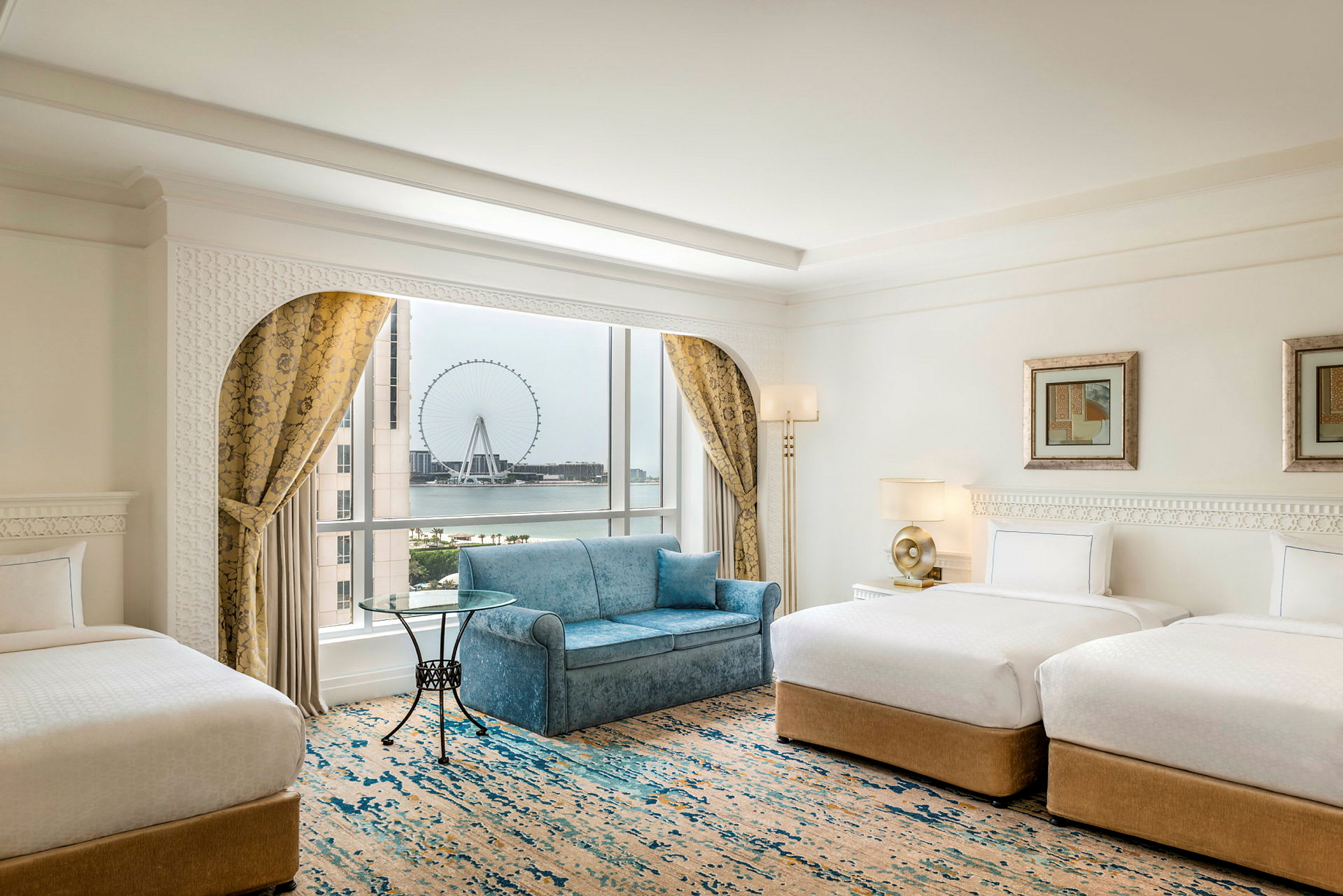 Et elegant hotelværelse med to enkeltsenge, en sofa, et vindue med udsigt til et stort pariserhjul og gardiner. (AI-genereret tekst)
