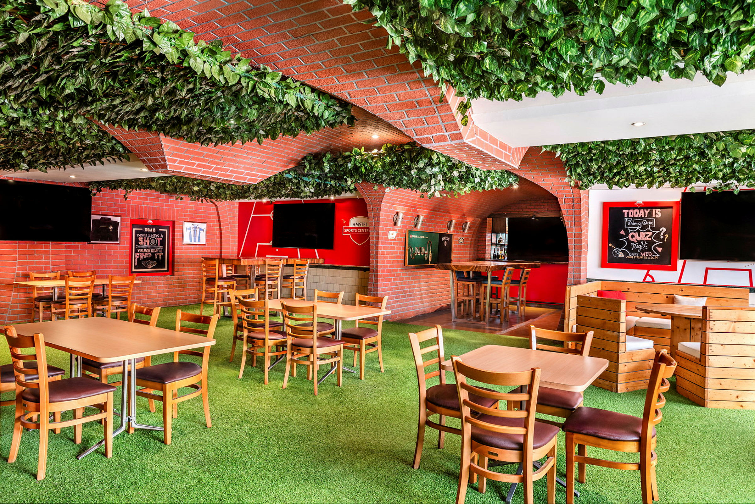 Interiør af en livlig restaurant med grønne vægge og loft. Træmøbler og en bar er indrettet med røde mursten. (AI-genereret tekst)