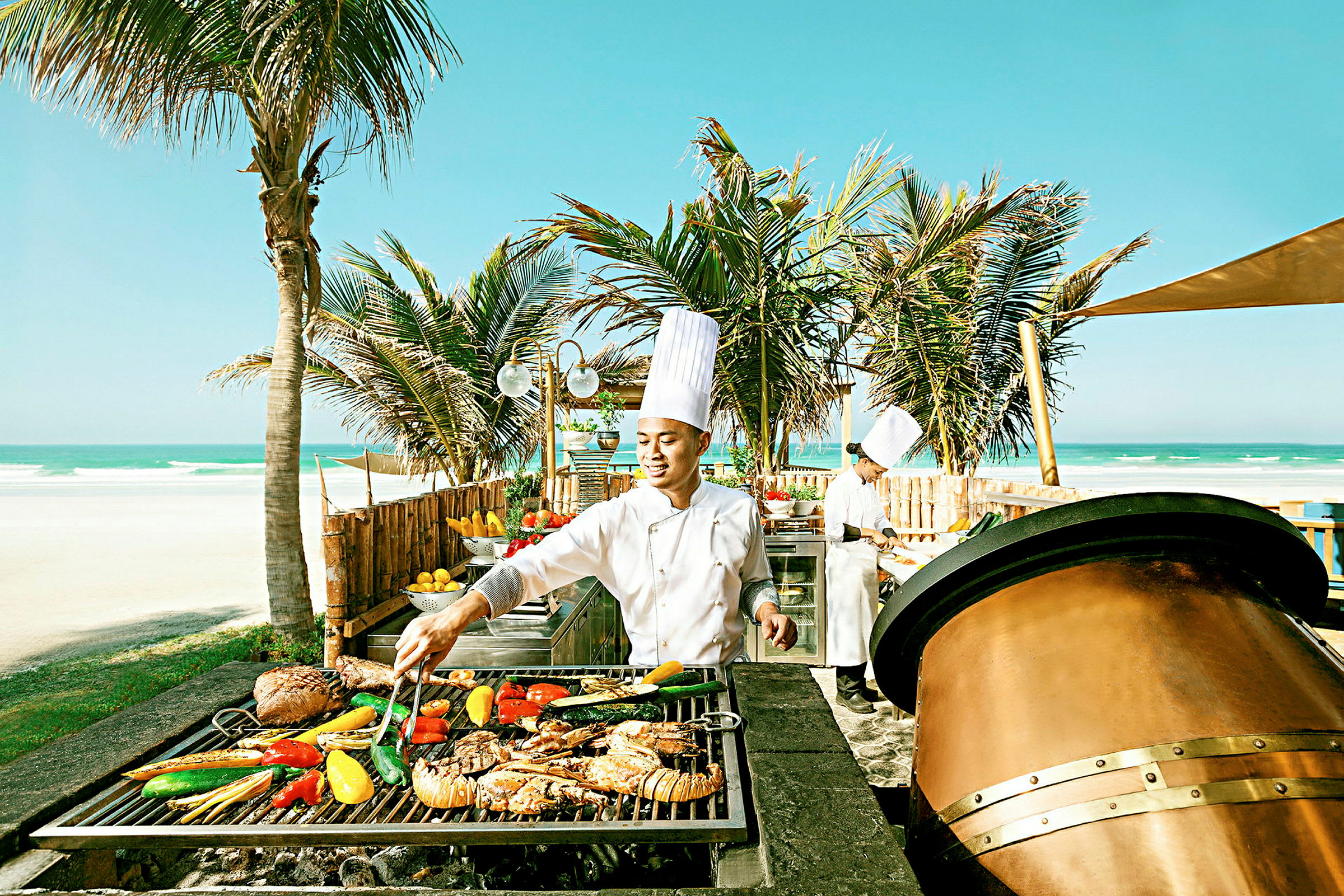 En kok ved en grillstation ved stranden med palmer i baggrunden. (AI-genereret tekst)