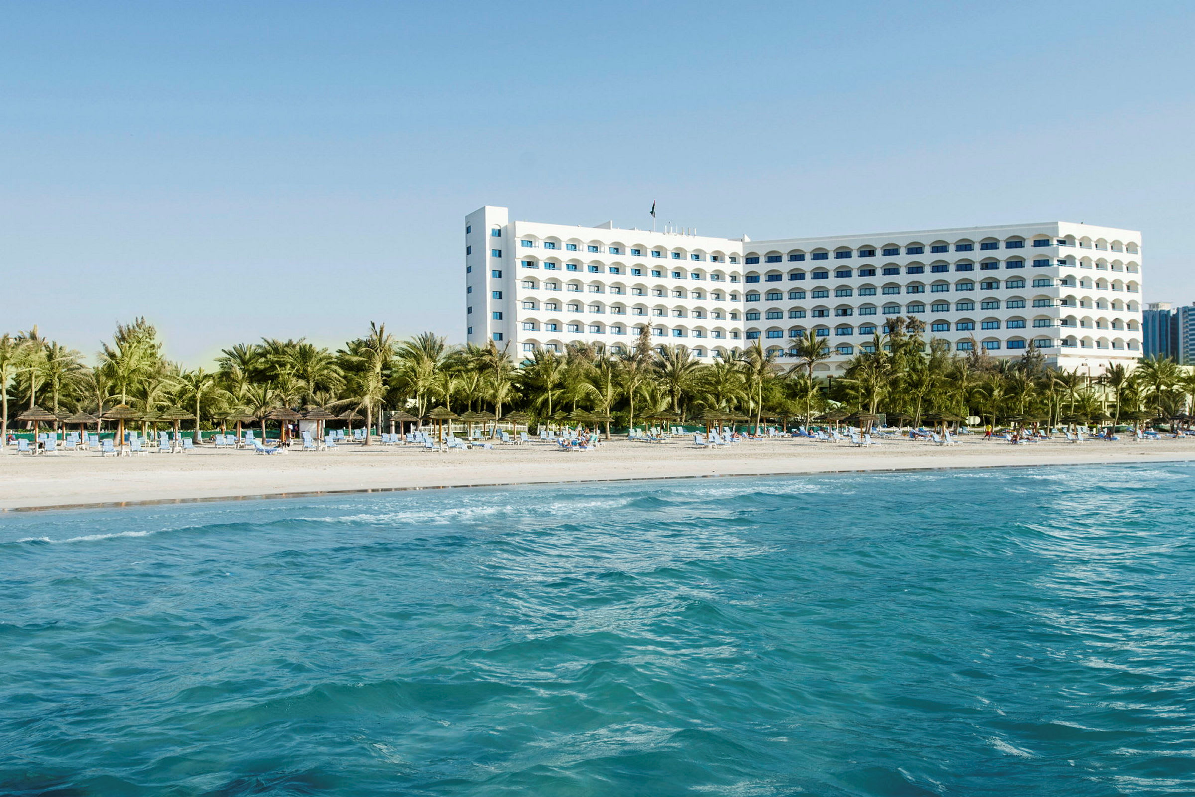 Hotel ved stranden med palmer og liggestole. (AI-genereret tekst)