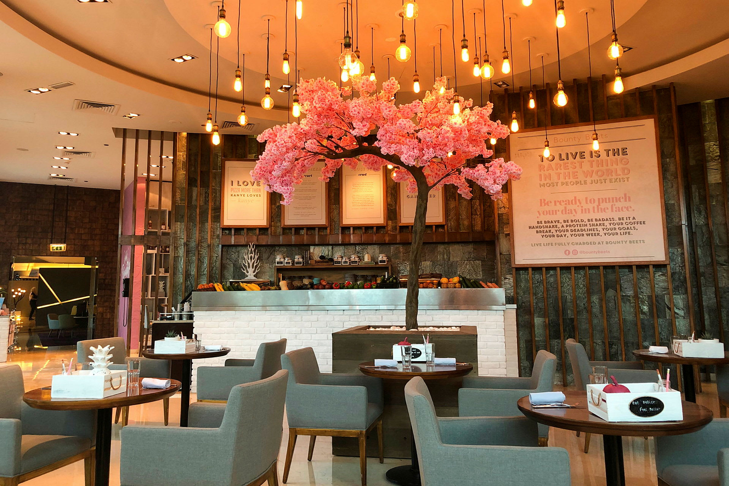 En restaurant med grå stole og borde, et dekorativt lyserødt blomstrende træ i midten. (AI-genereret tekst)